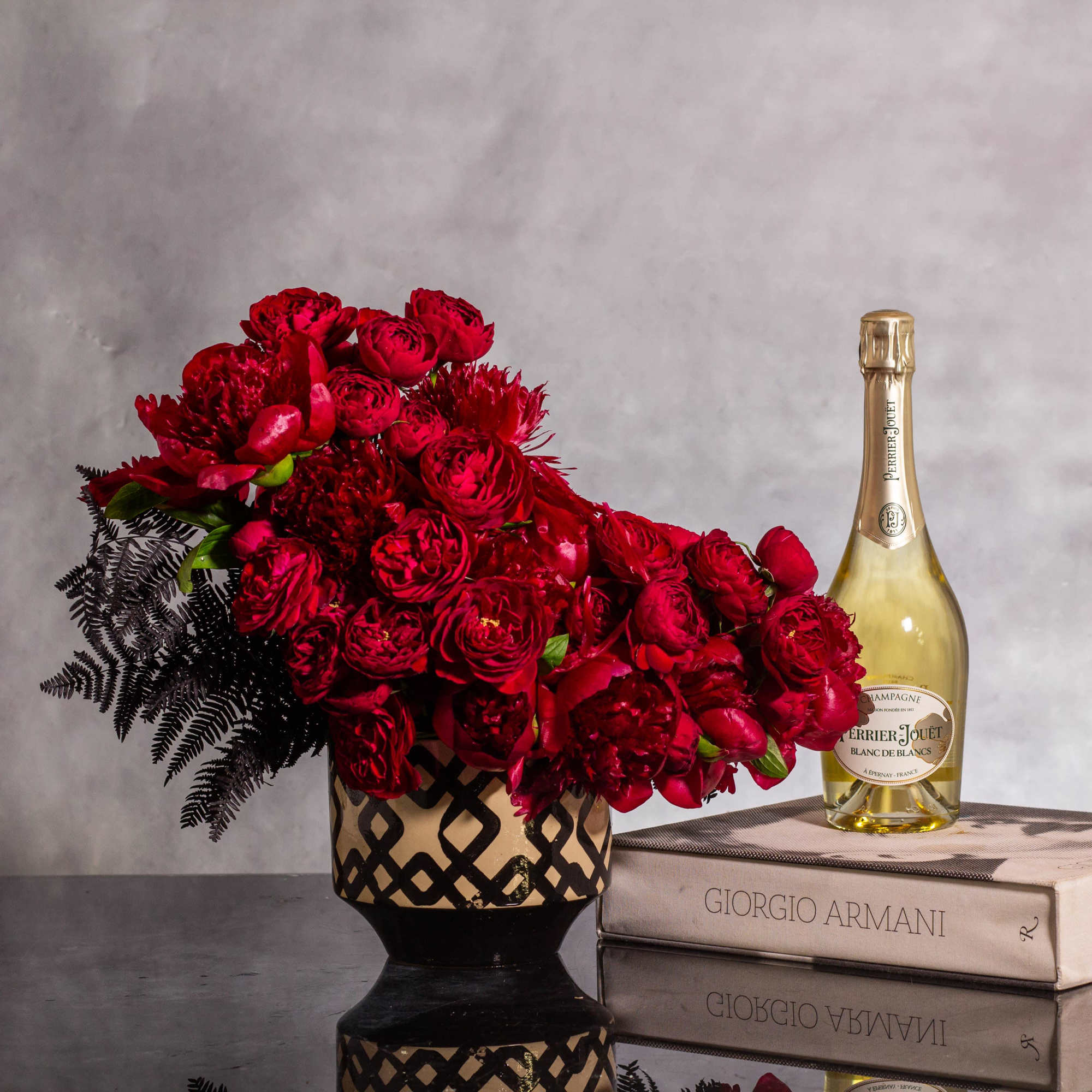 Red rose bouquet in a patterned vase beside a champagne bottle