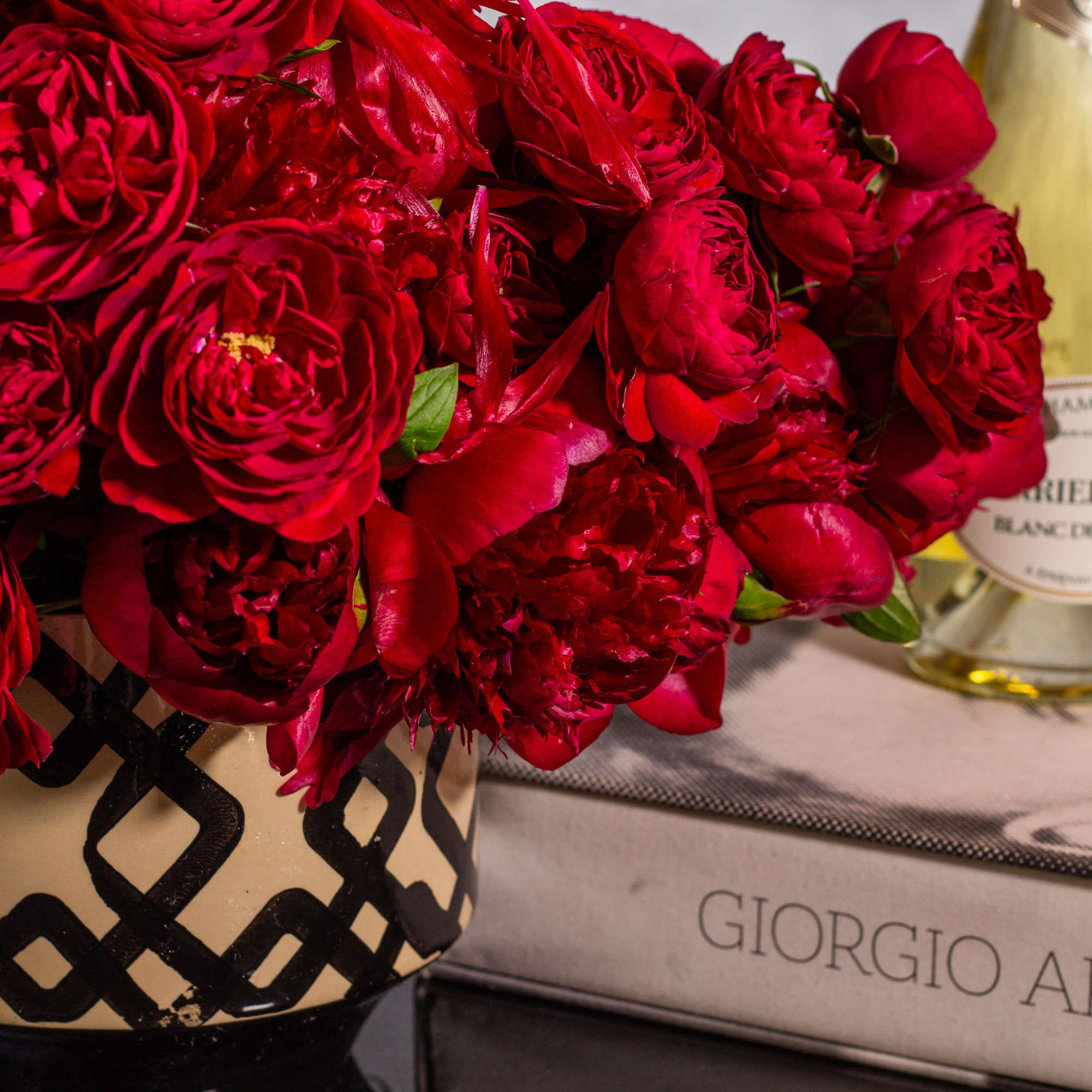 Red rose bouquet in a patterned vase beside a bottle of champagne