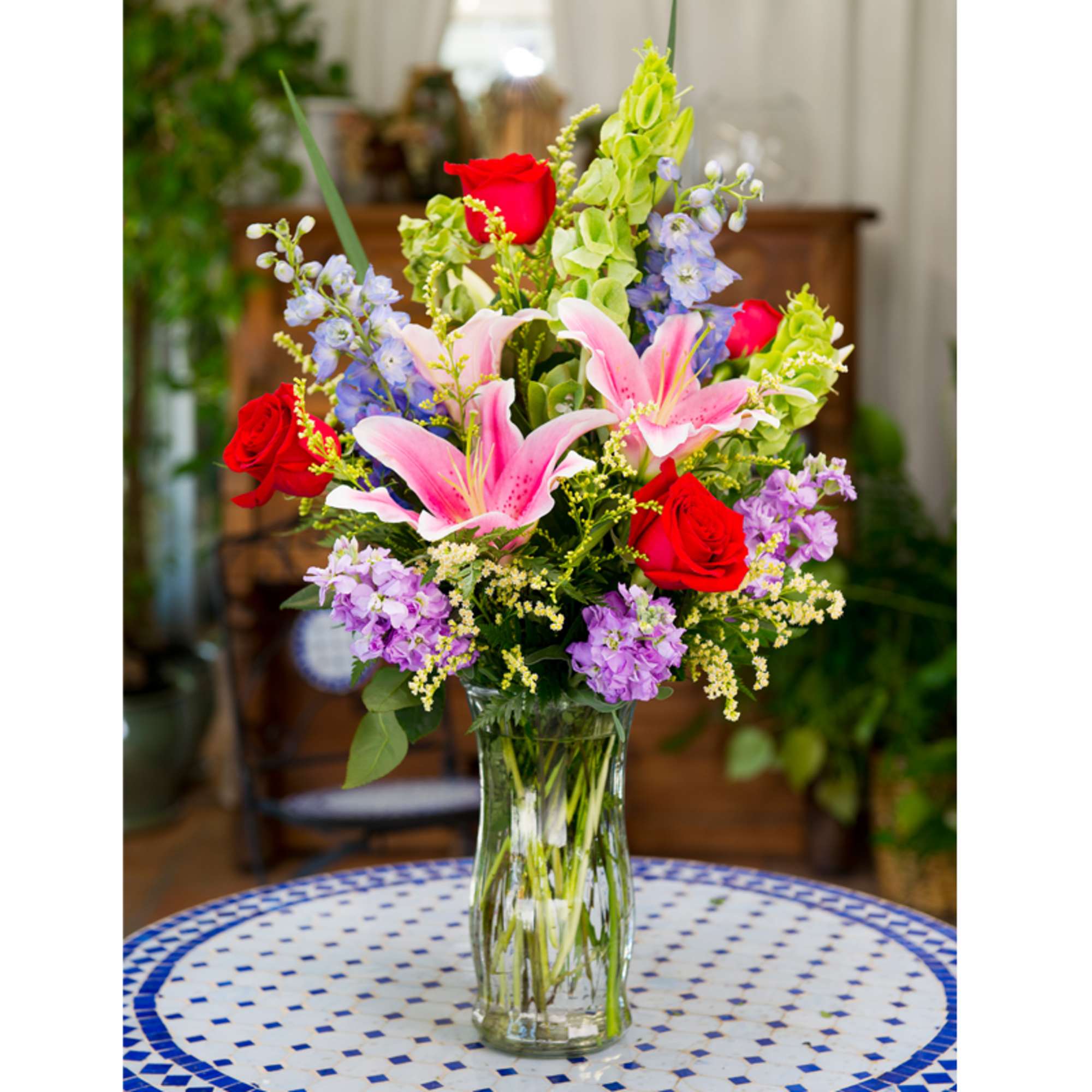 Bouquet of red roses, pink lilies, and purple flowers in a glass vase