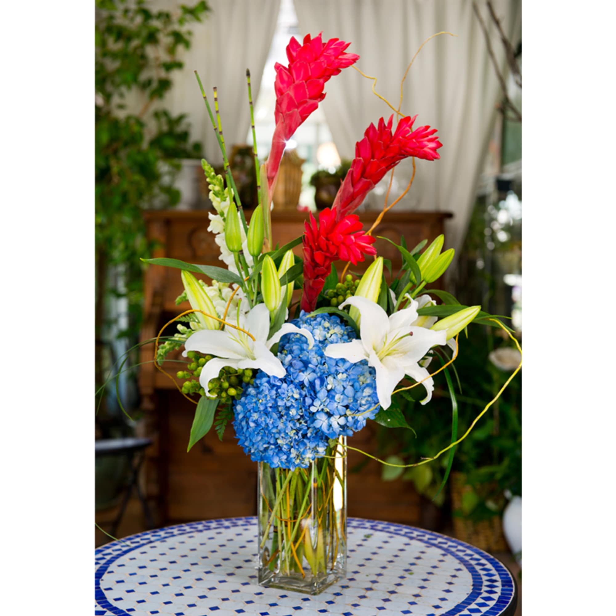 Tall vase arrangement with blue hydrangea, white lilies, and red tropical blooms, photo 2 of 2