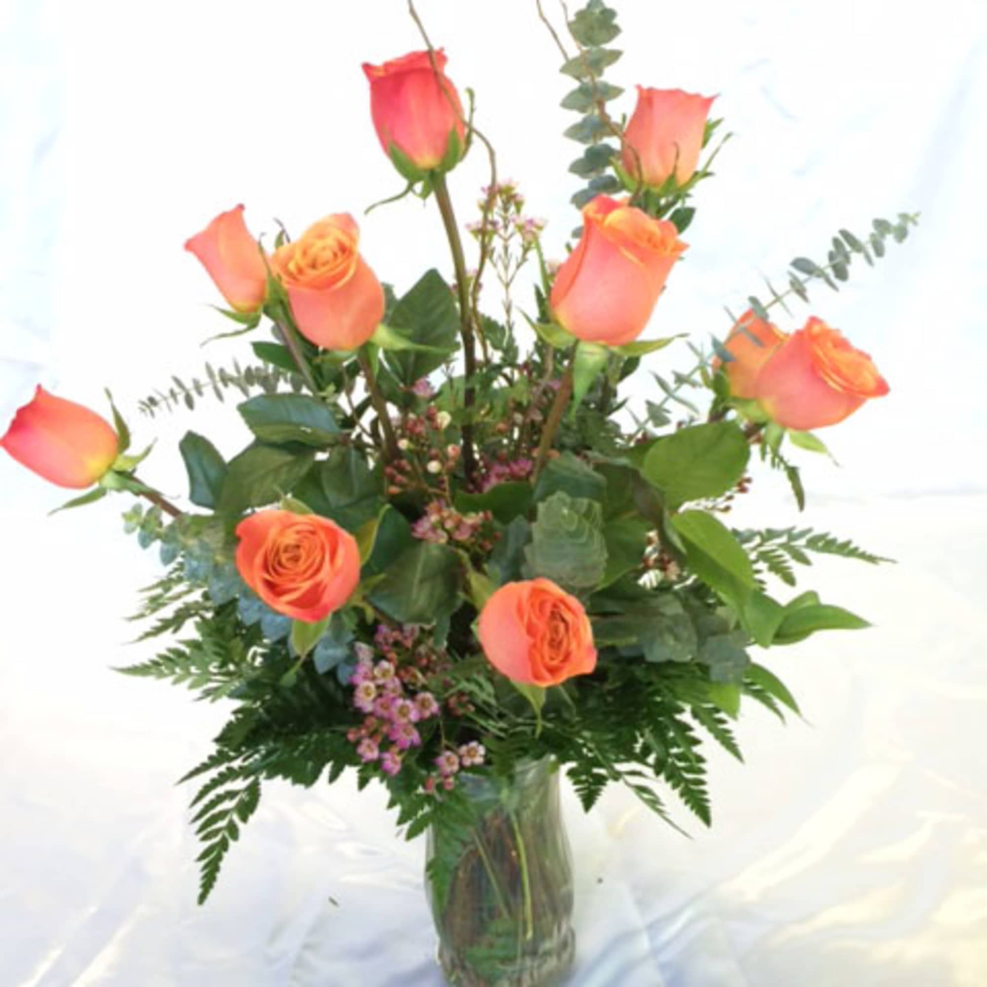 Orange roses arranged in a clear glass vase with greenery, photo 2 of 2