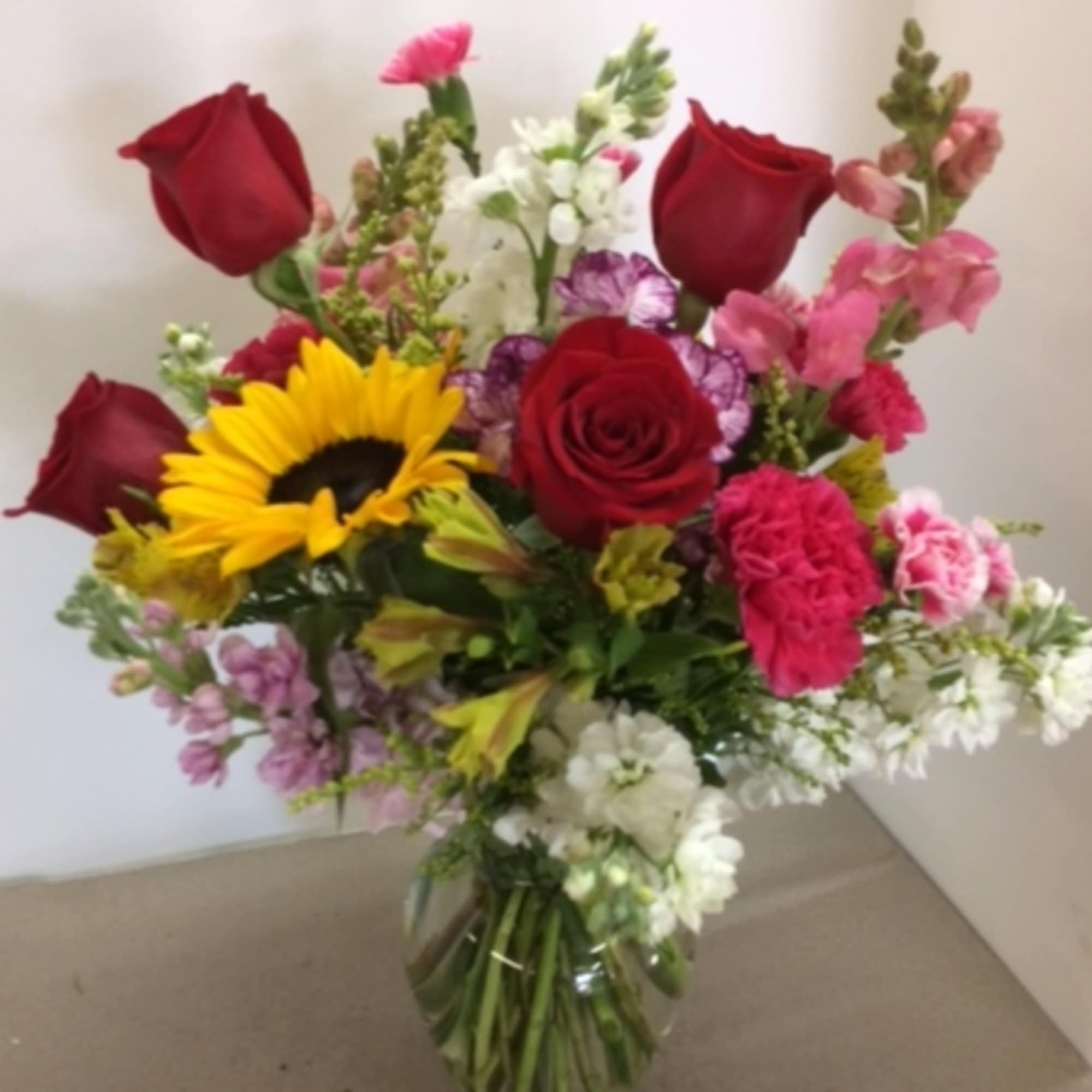 Mixed bouquet of red roses, a sunflower, and pink blooms in a glass vase