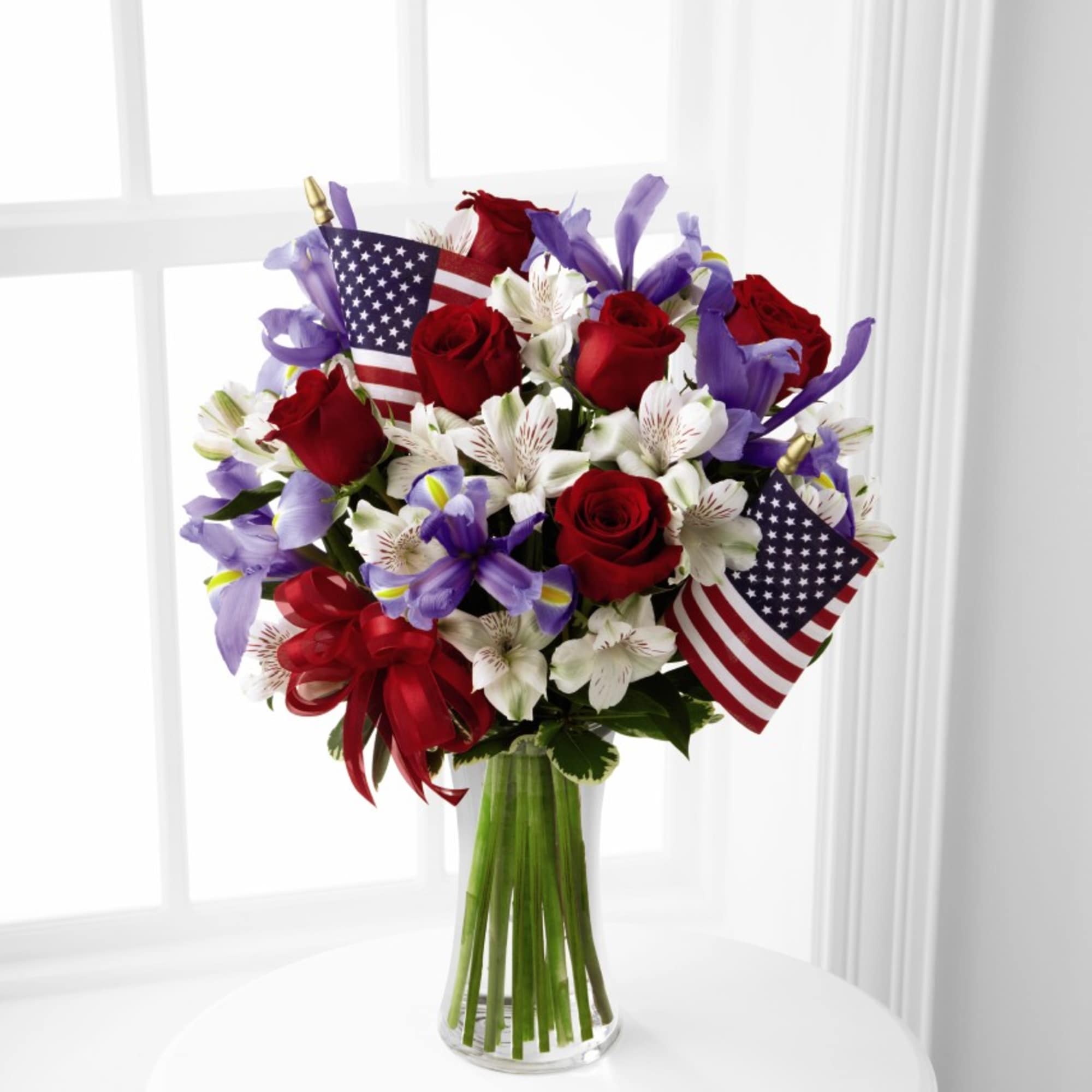 Bouquet of red roses and white-purple flowers in a glass vase with small American flags