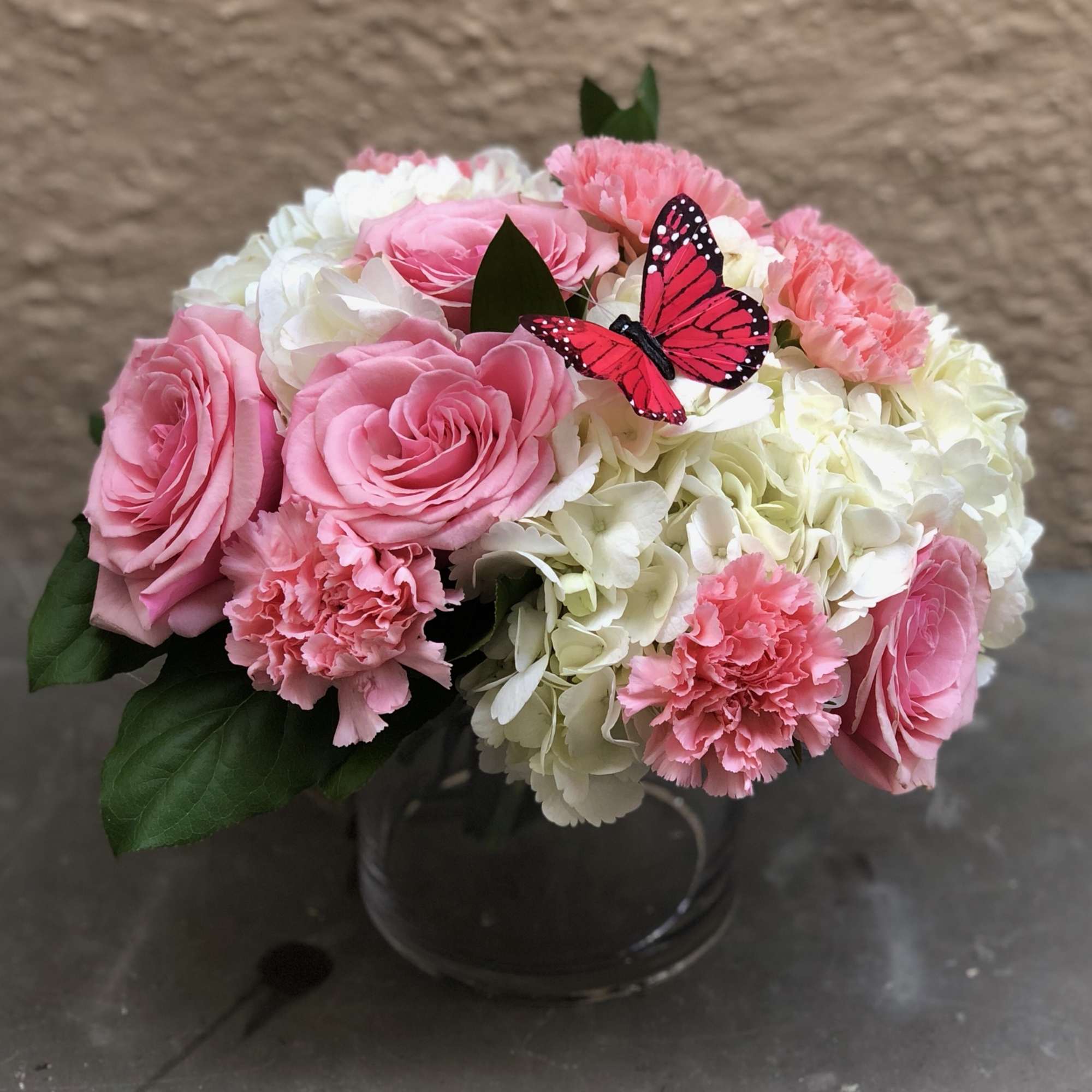 Pink roses and carnations in a glass vase with a butterfly accent