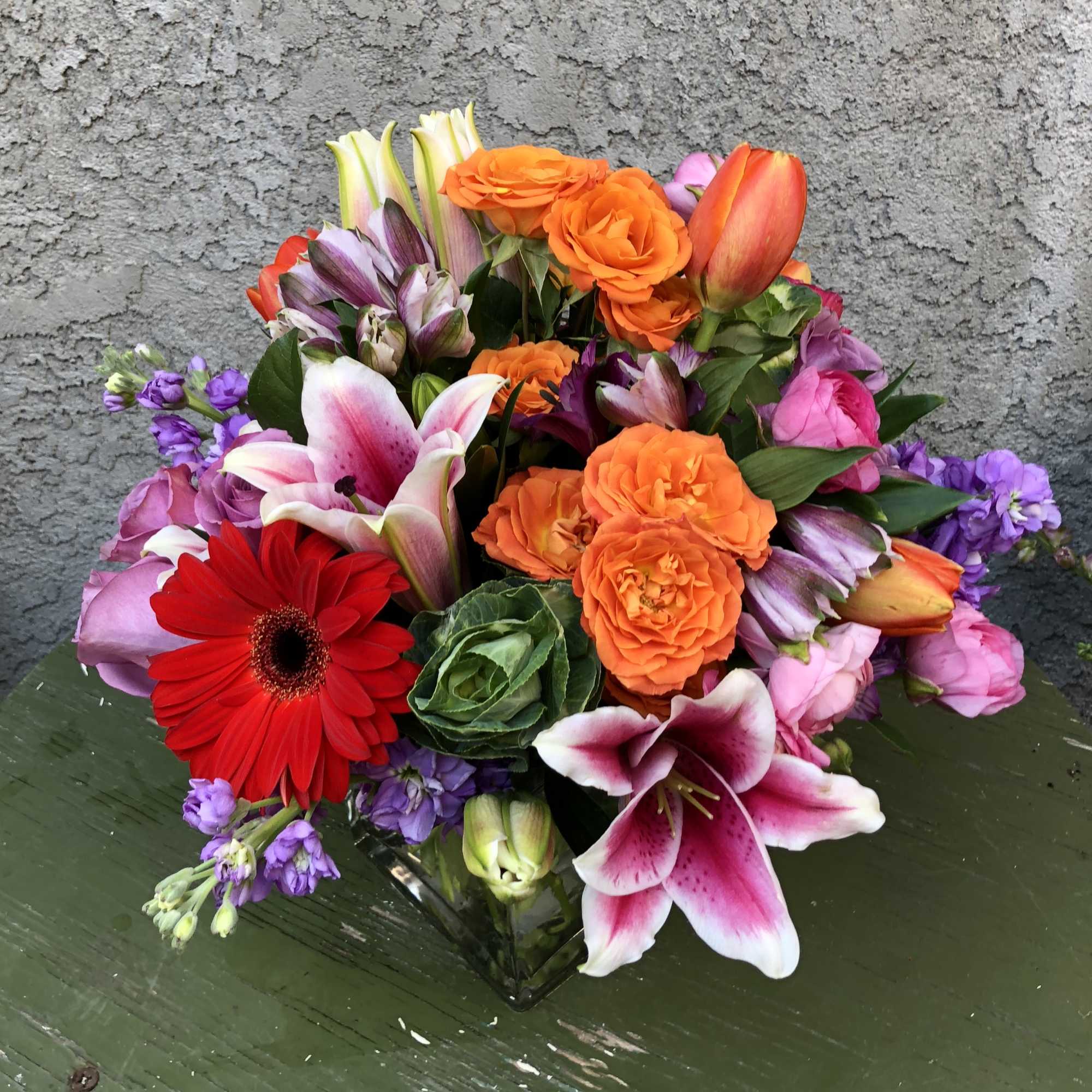 Mixed bouquet with orange roses, pink lilies, and a red gerbera daisy in a glass vase