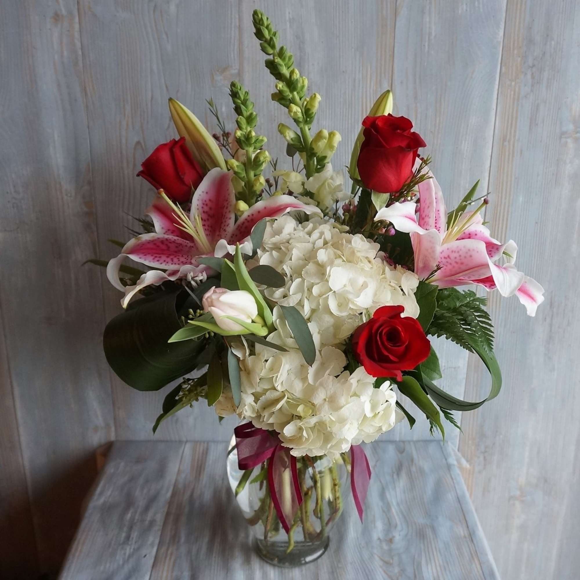 Bouquet of red roses, pink lilies, and white hydrangeas in a glass vase
