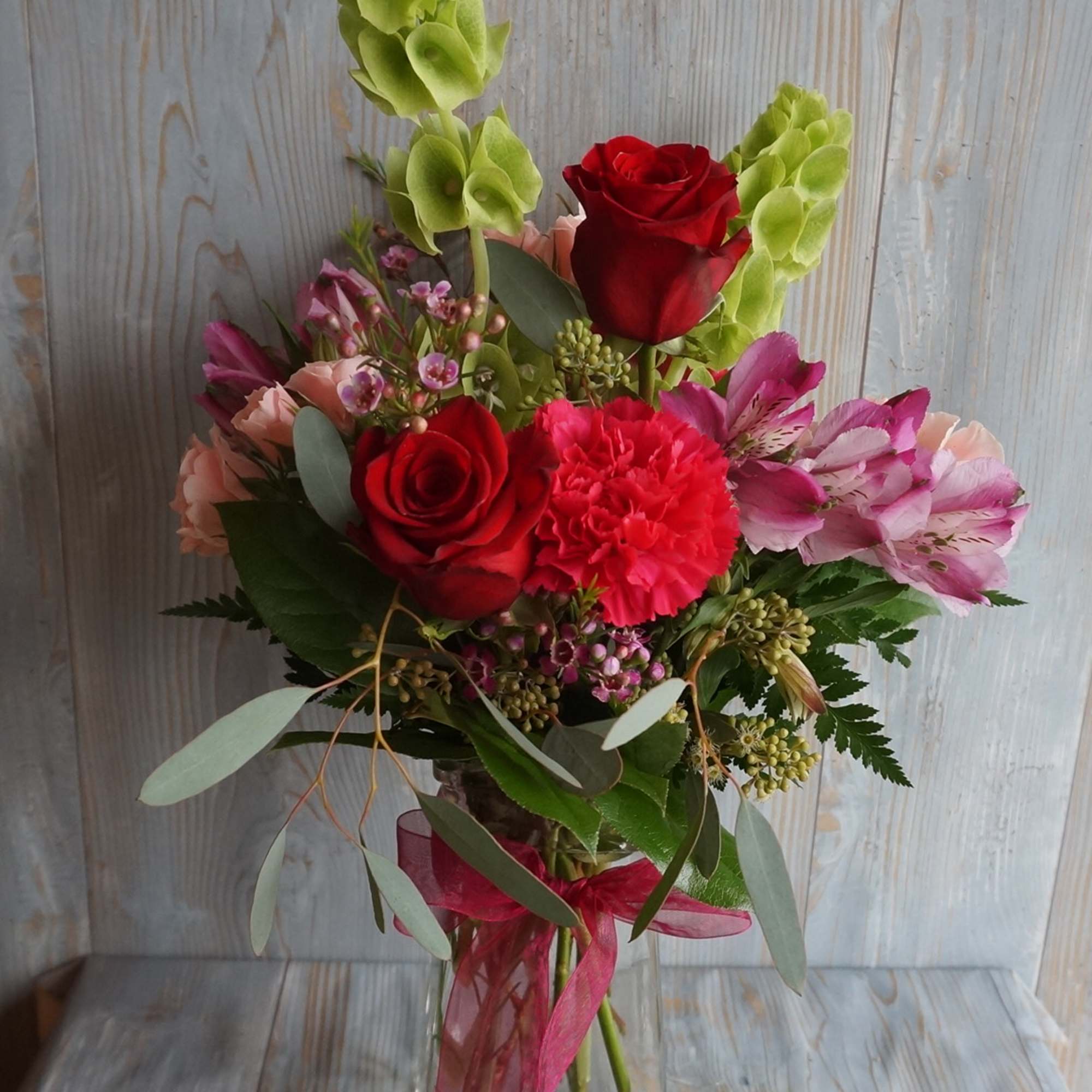 Bouquet of red roses, pink carnations, and green orchids in a glass vase
