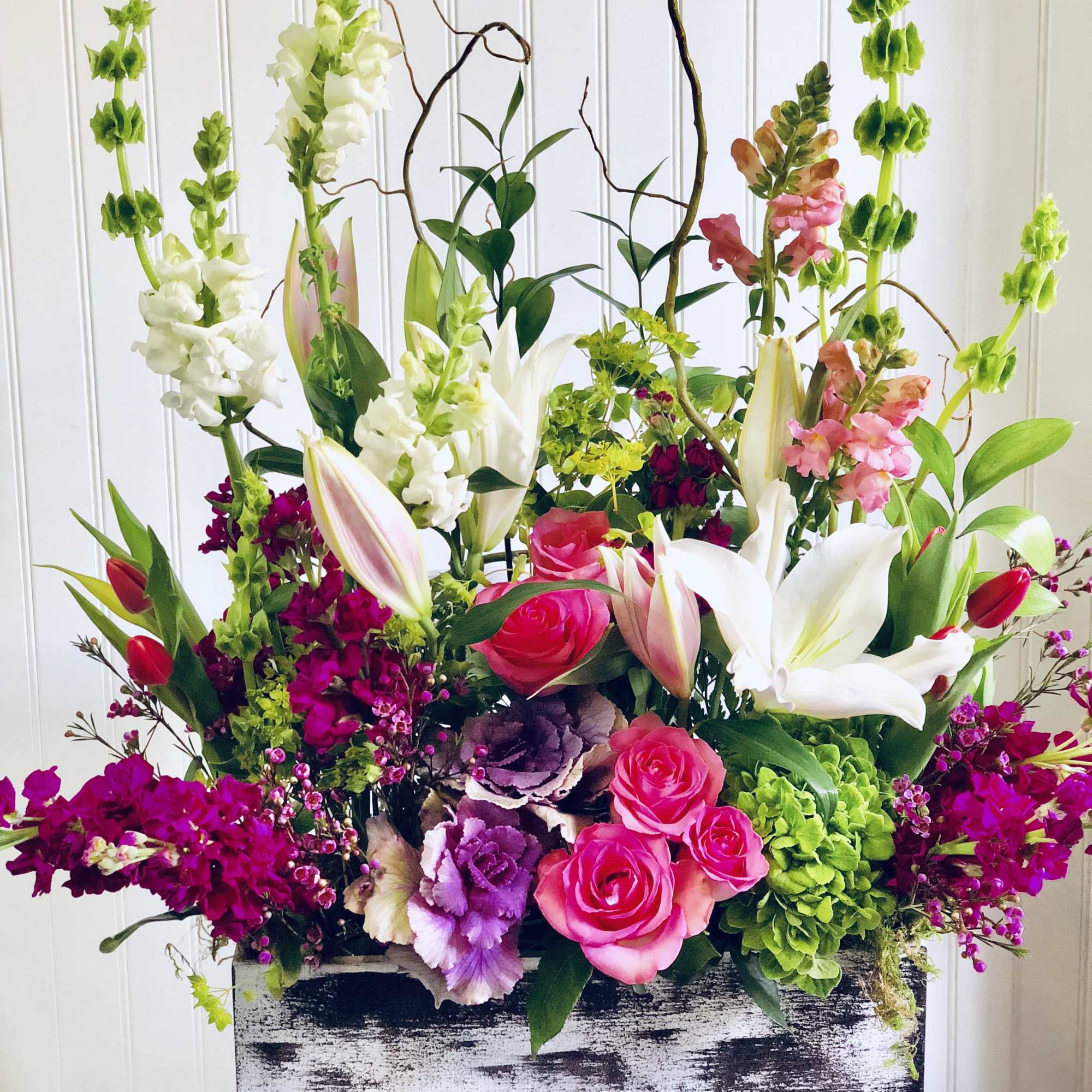 Tall mixed floral arrangement with pink roses, white lilies, and green blooms in a rustic box