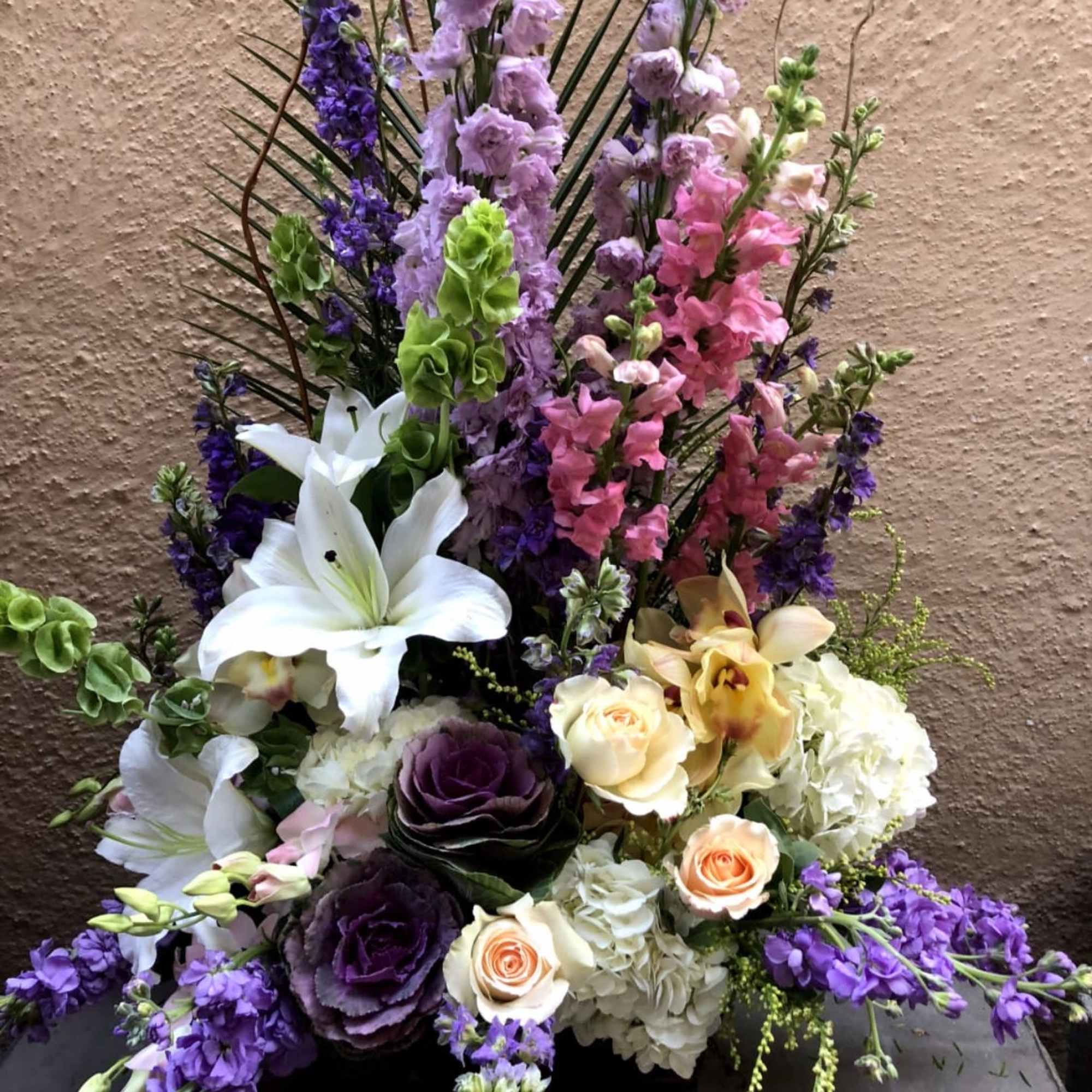Tall floral arrangement with lilies, roses, hydrangeas, and purple blooms