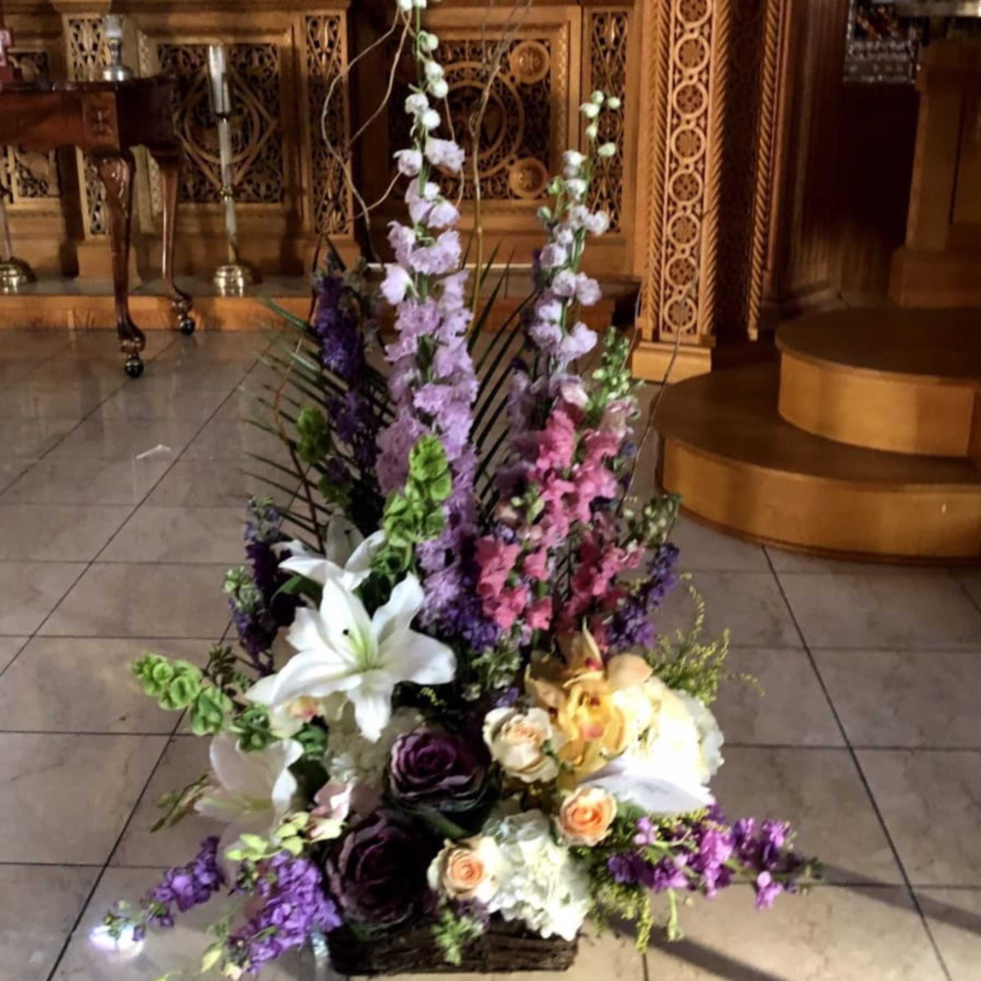 Tall floral arrangement with lilies, roses, and purple blooms in a basket