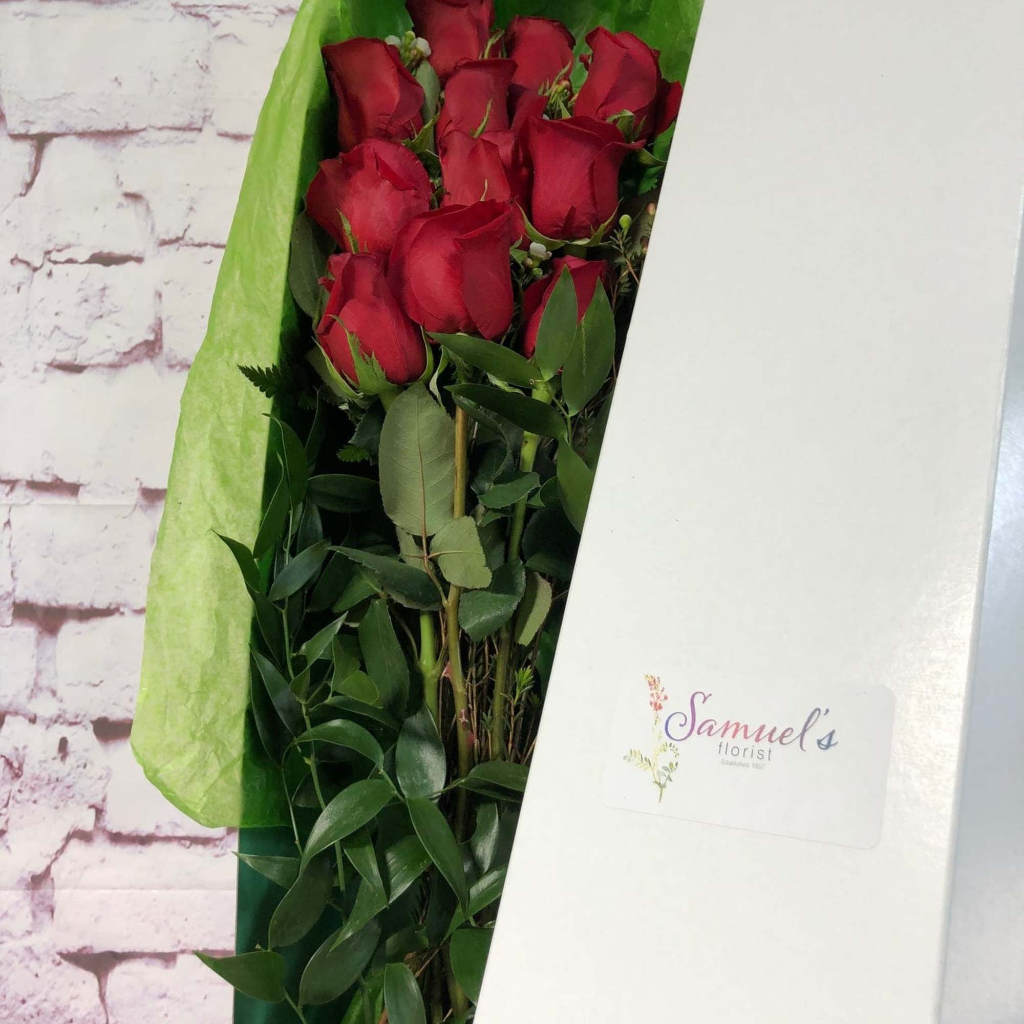 Bouquet of red roses wrapped in green paper inside a white box
