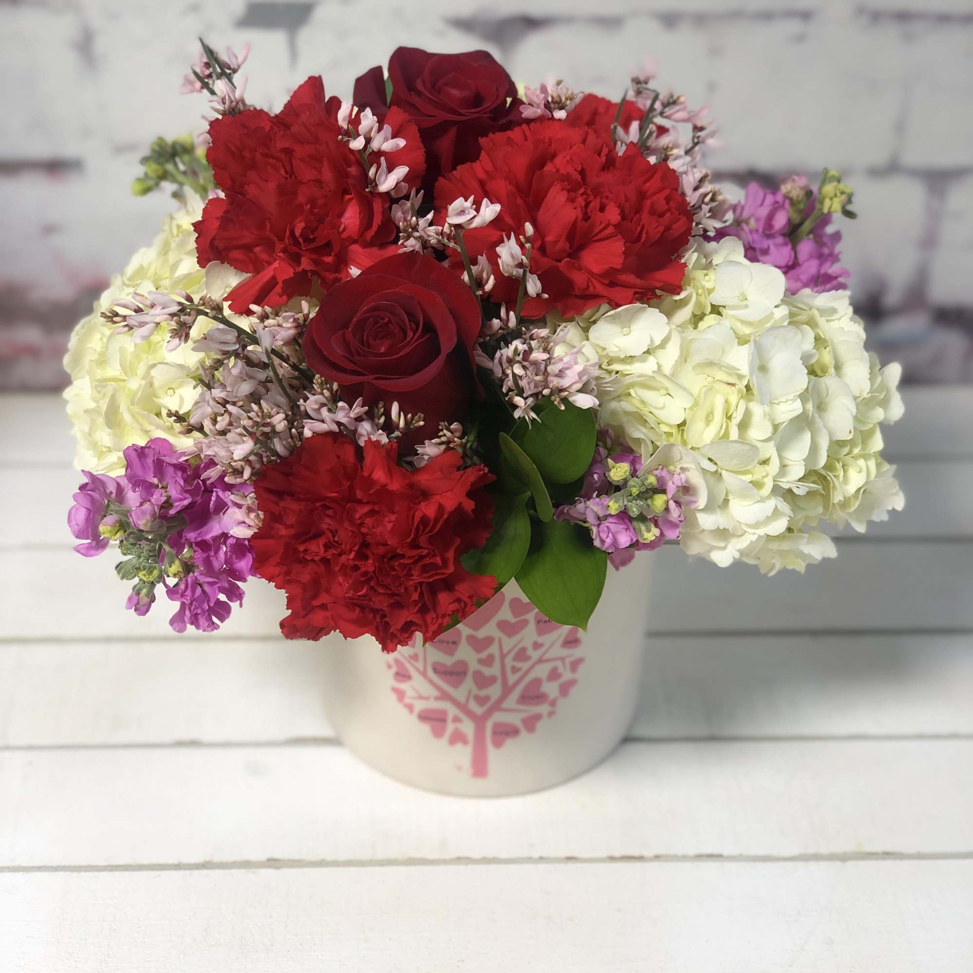 Bouquet of red roses, red carnations, and white hydrangeas in a white container