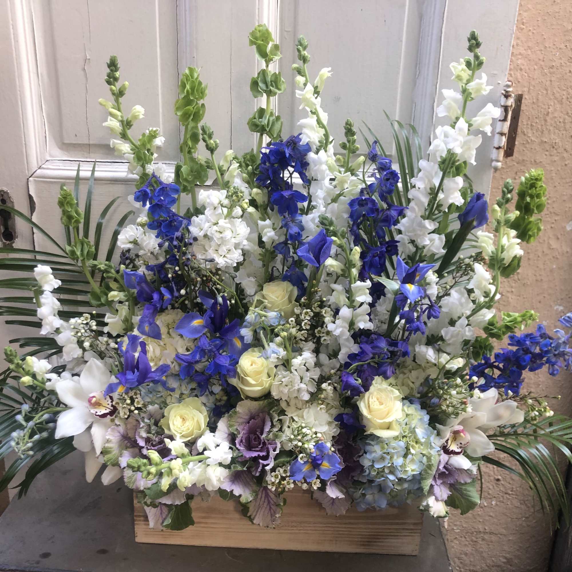 Large blue, white, and pale yellow floral arrangement in a wooden box