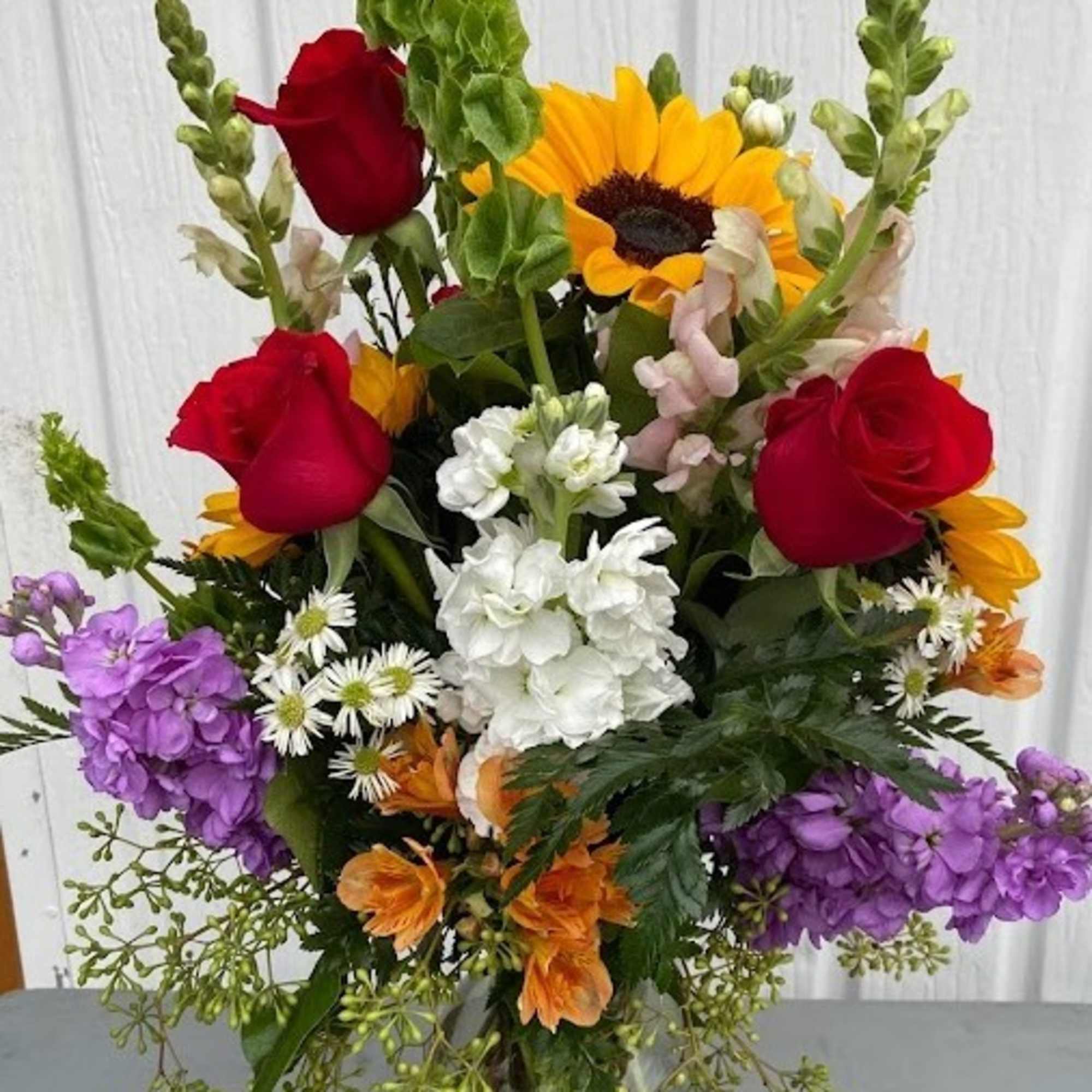 Mixed bouquet with red roses, a sunflower, white blooms, and purple flowers in a glass vase