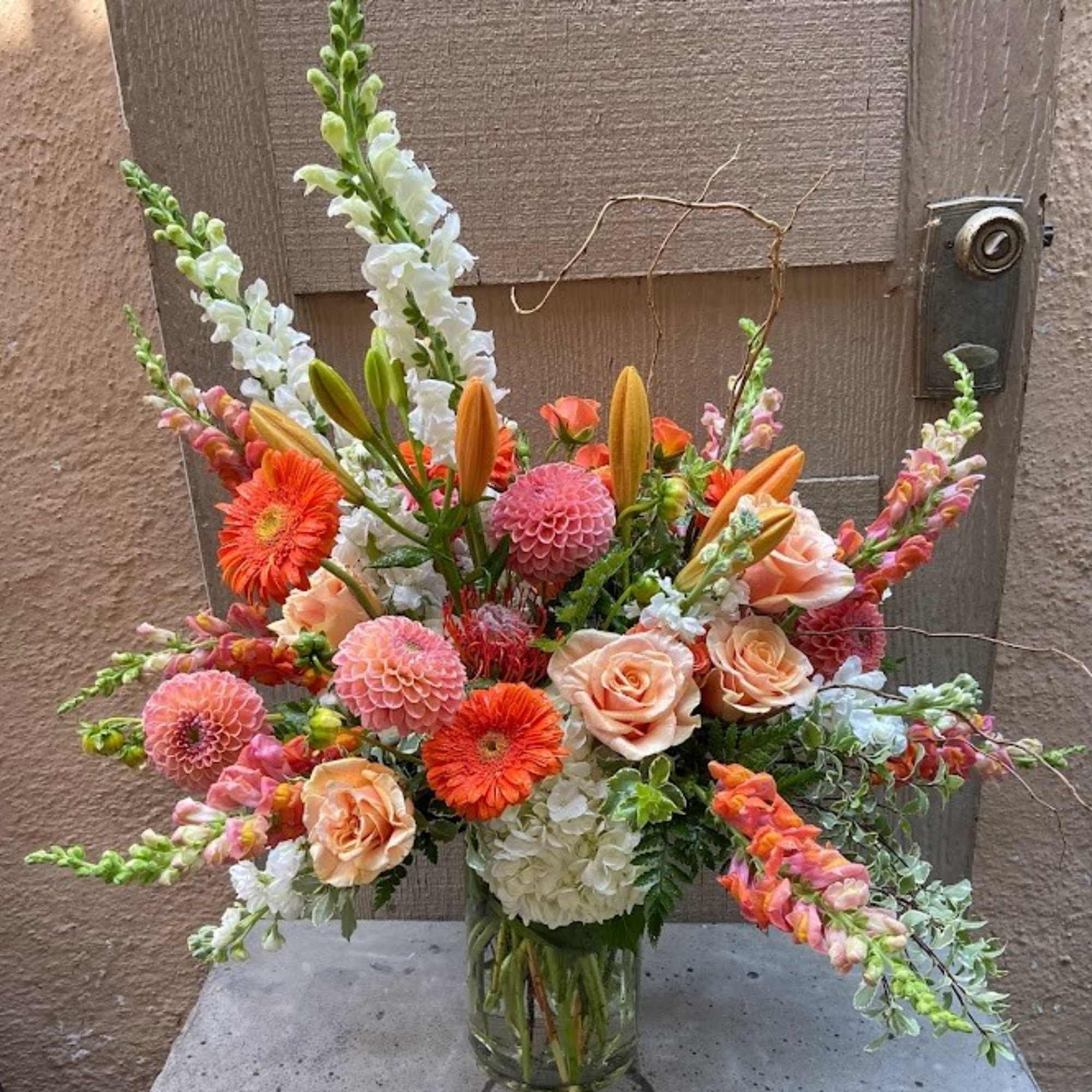 Mixed bouquet of peach roses, orange gerberas, and pink blooms in a glass vase