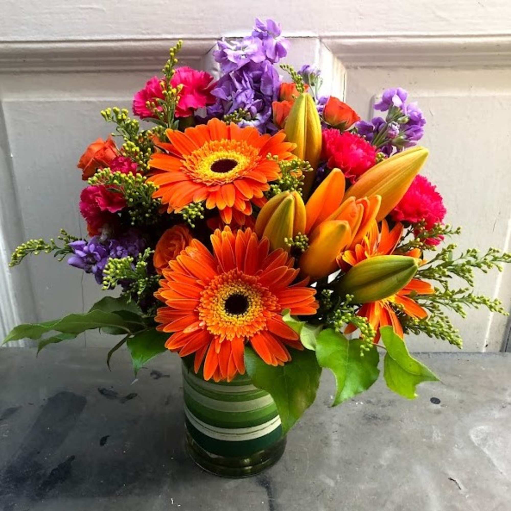 Bright mixed bouquet with orange gerbera daisies and lilies in a striped vase
