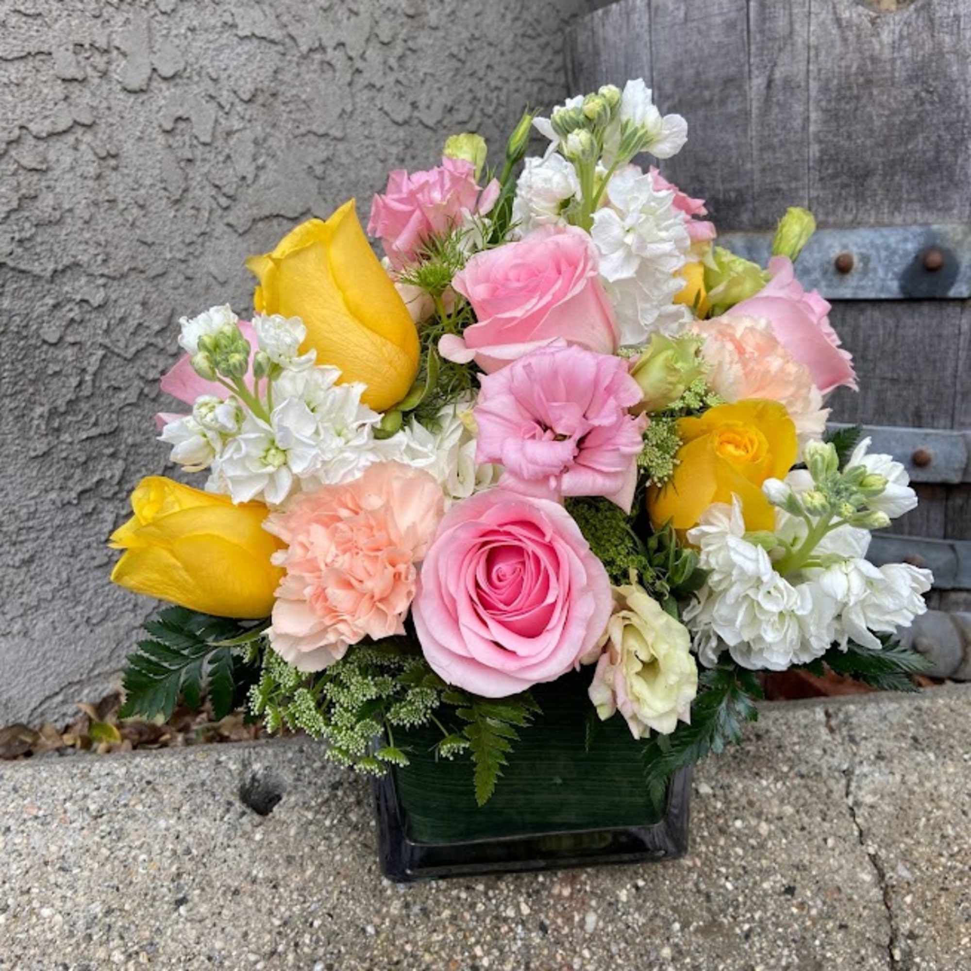 Bouquet of pink and yellow roses with white blooms in a square vase