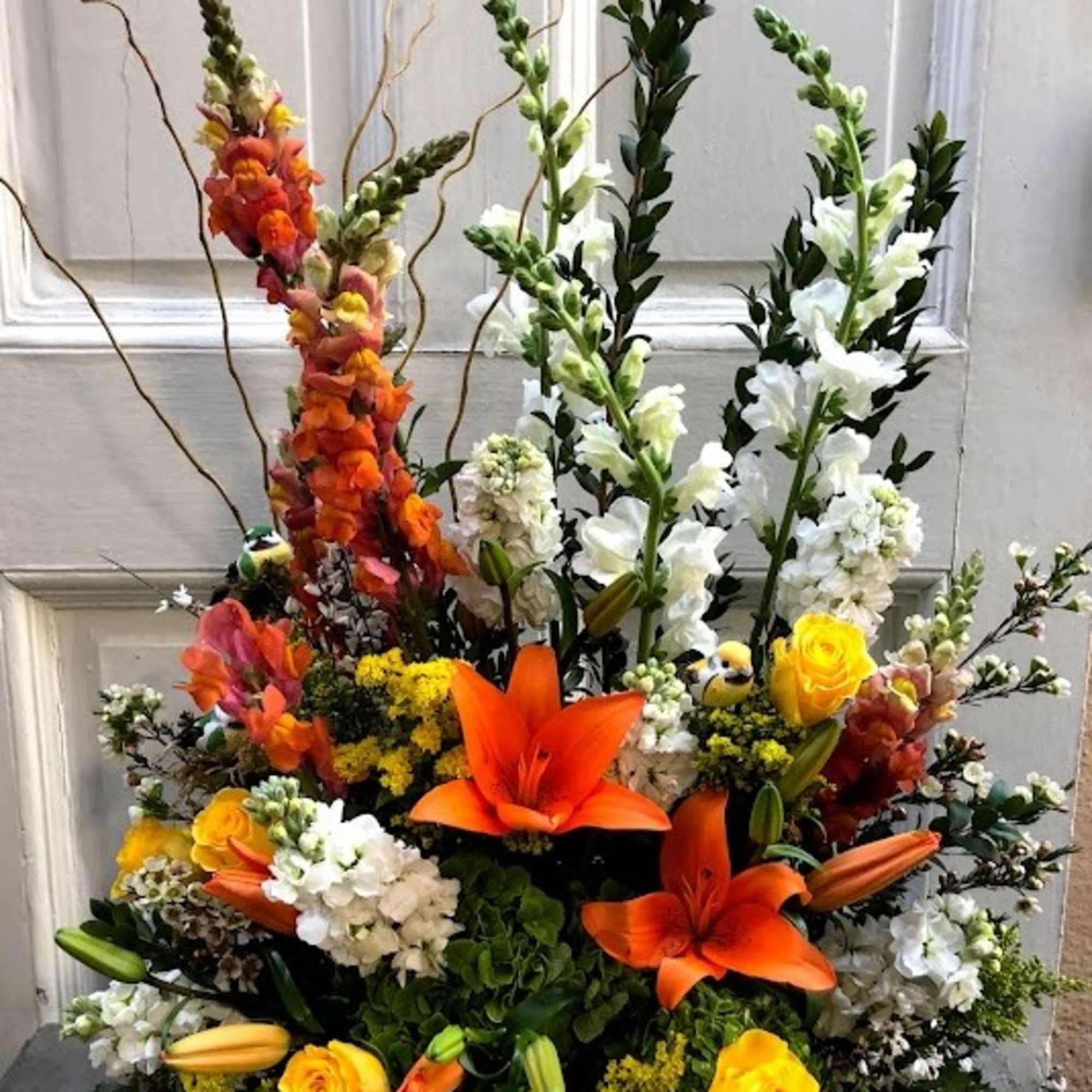 Tall floral arrangement with orange lilies, yellow roses, and white snapdragons
