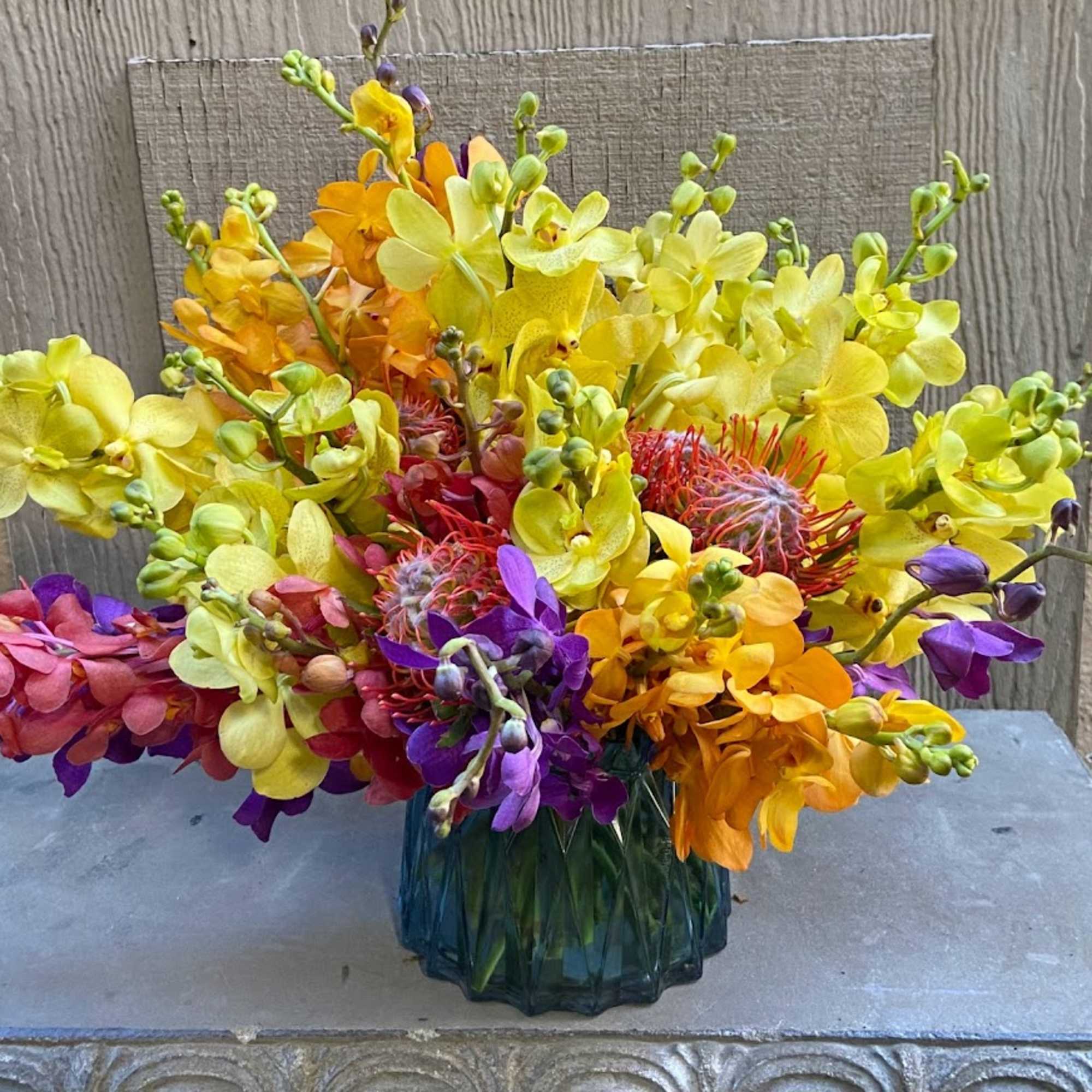 Bright orchid arrangement in a blue glass vase