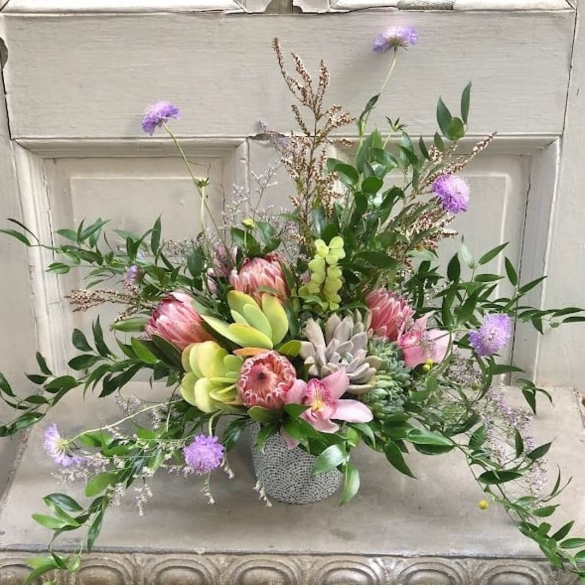 Mixed bouquet with pink protea, orchids, and purple blooms in a small vase