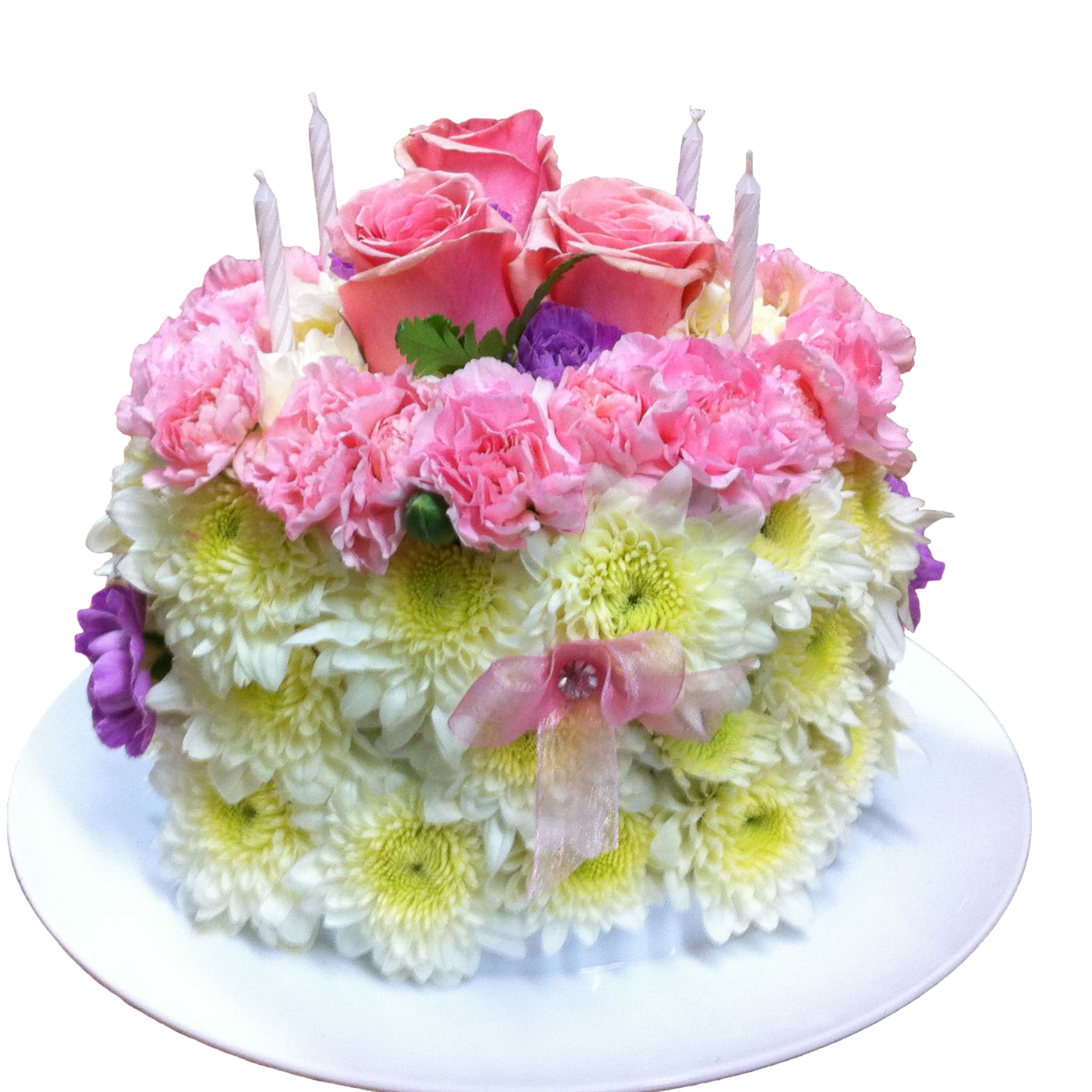 Round floral cake of white mums with pink carnations and roses, decorated with candles on a white plate.