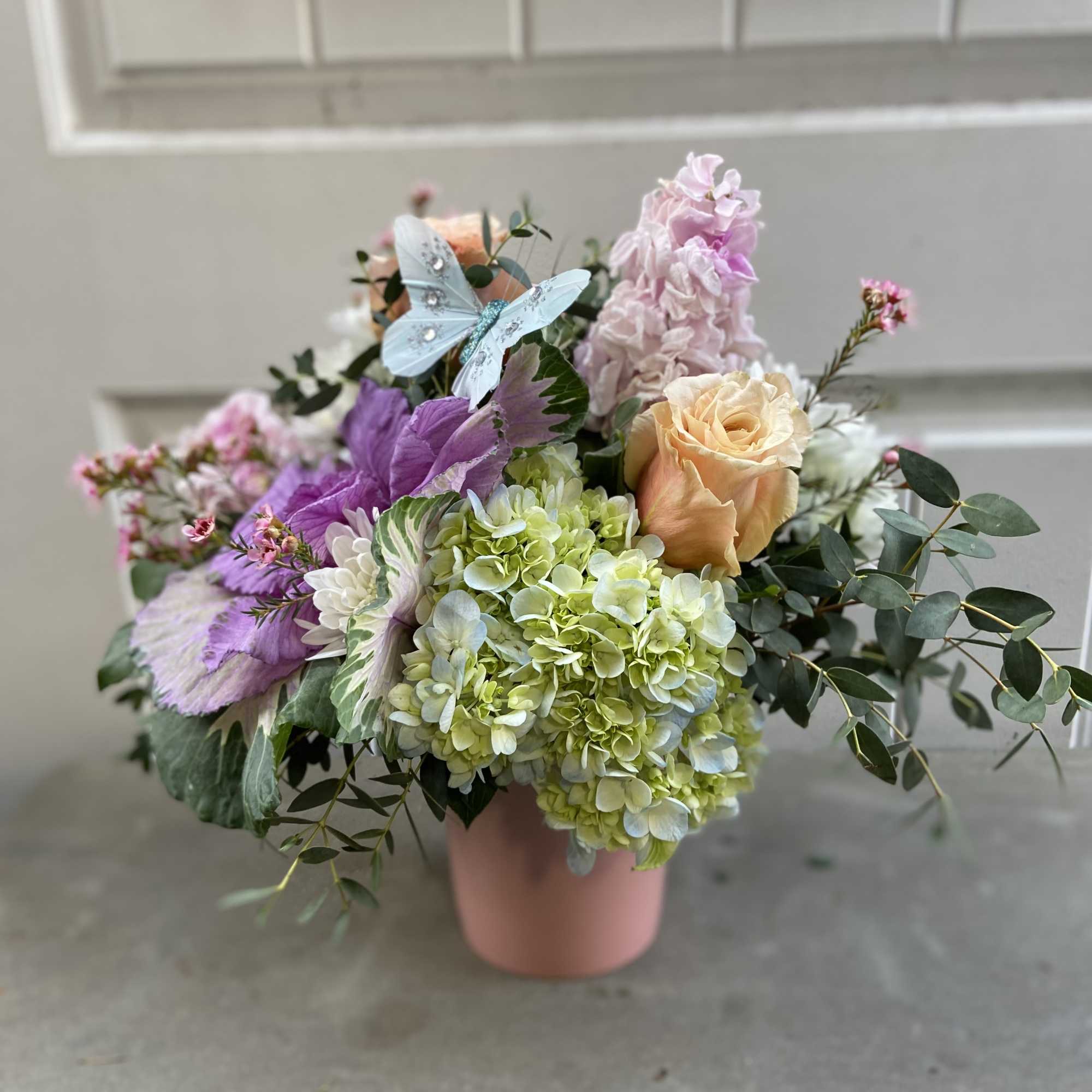 Pastel bouquet in a pink vase with roses, hydrangeas, and a butterfly decoration