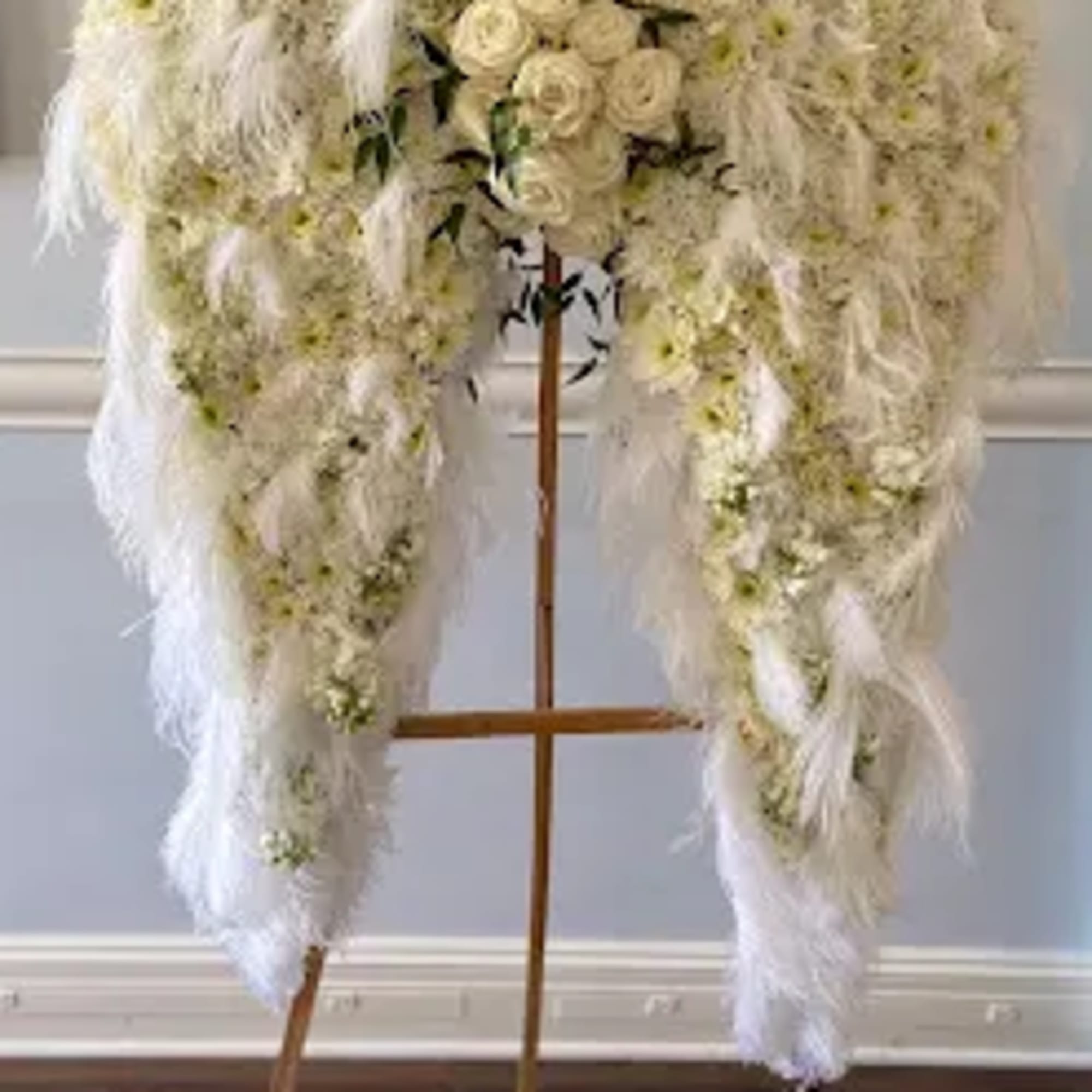 White floral funeral spray on a wooden stand with cascading feathers