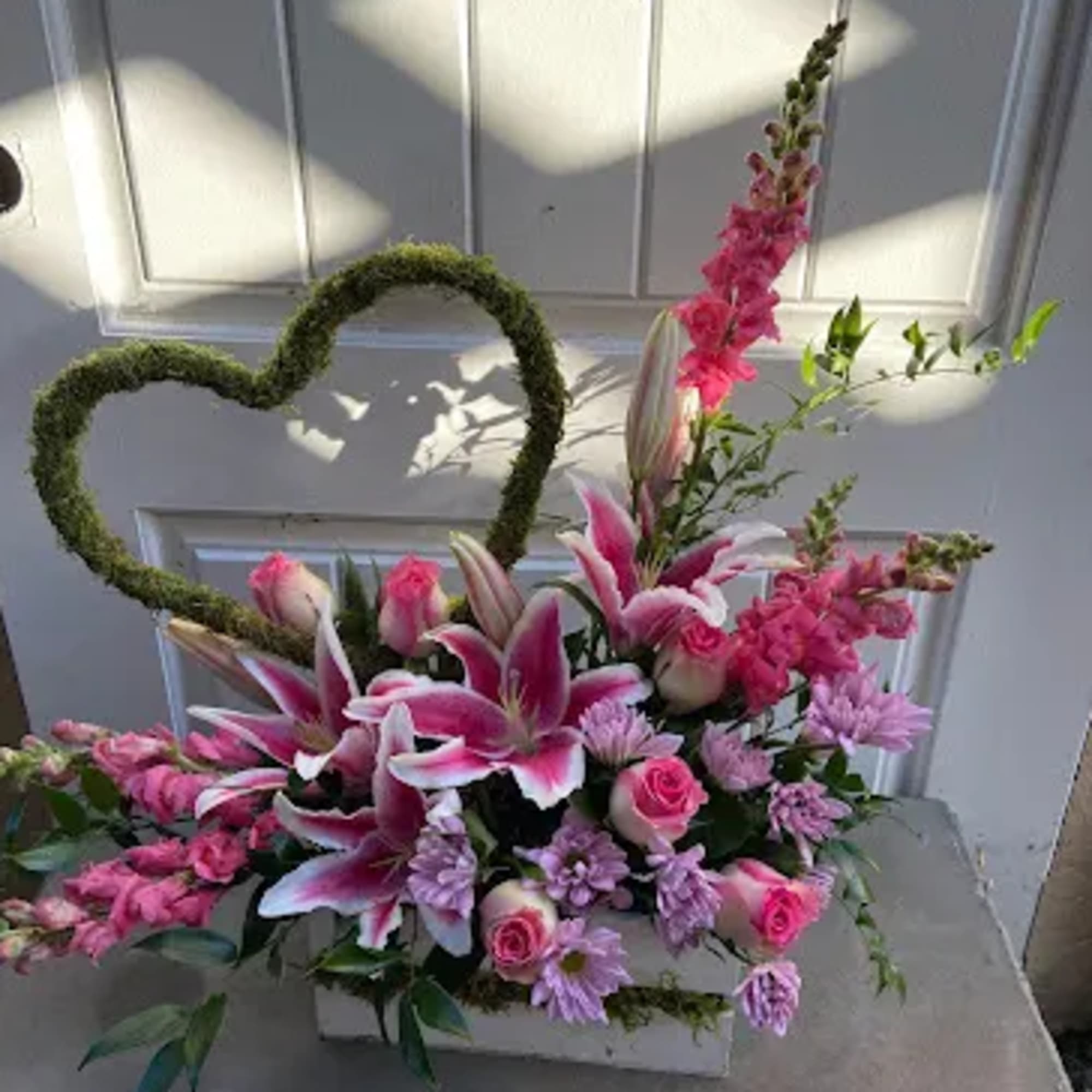Pink and white floral arrangement with a moss heart frame in a white box
