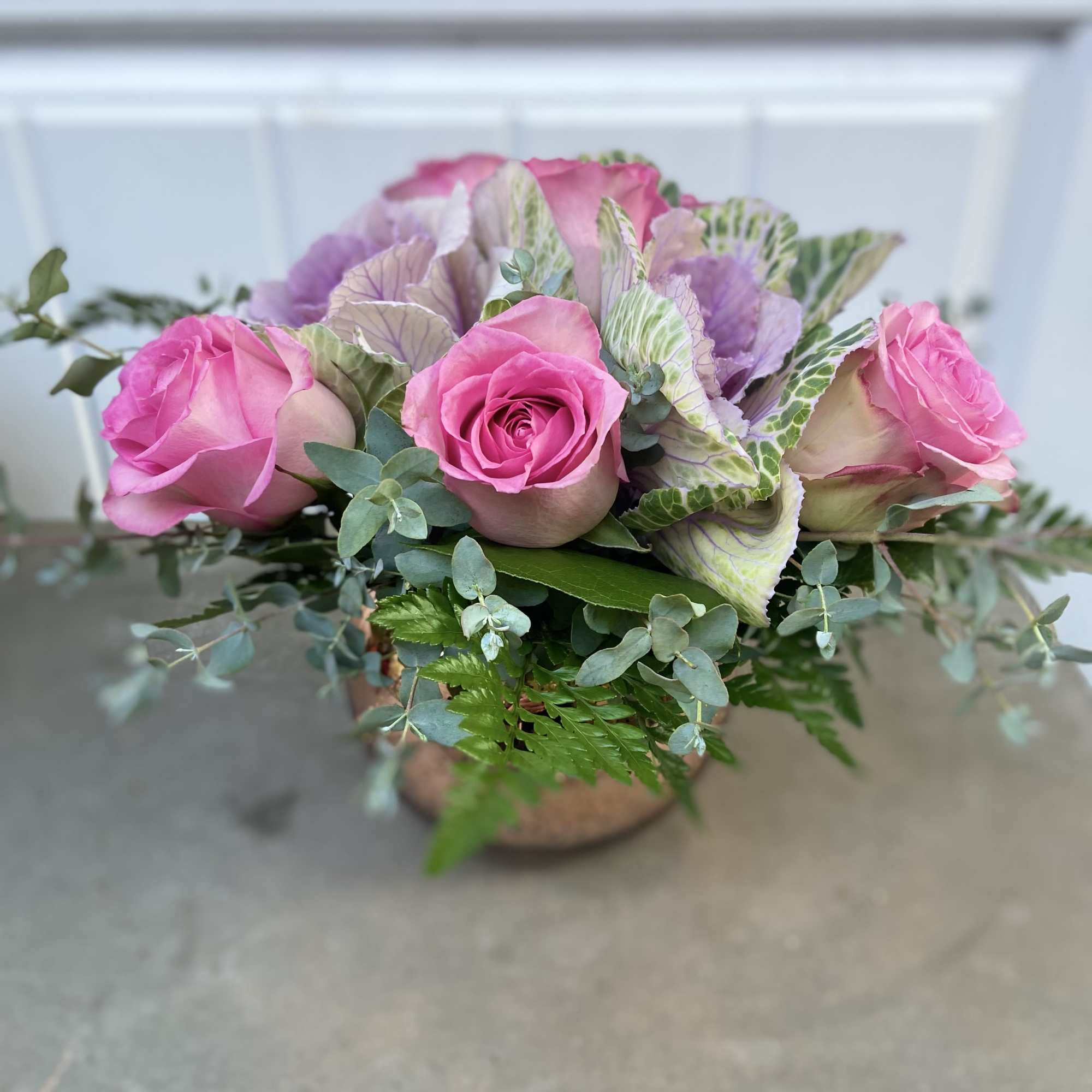 Pink roses arranged with pale purple cabbage leaves in a low container