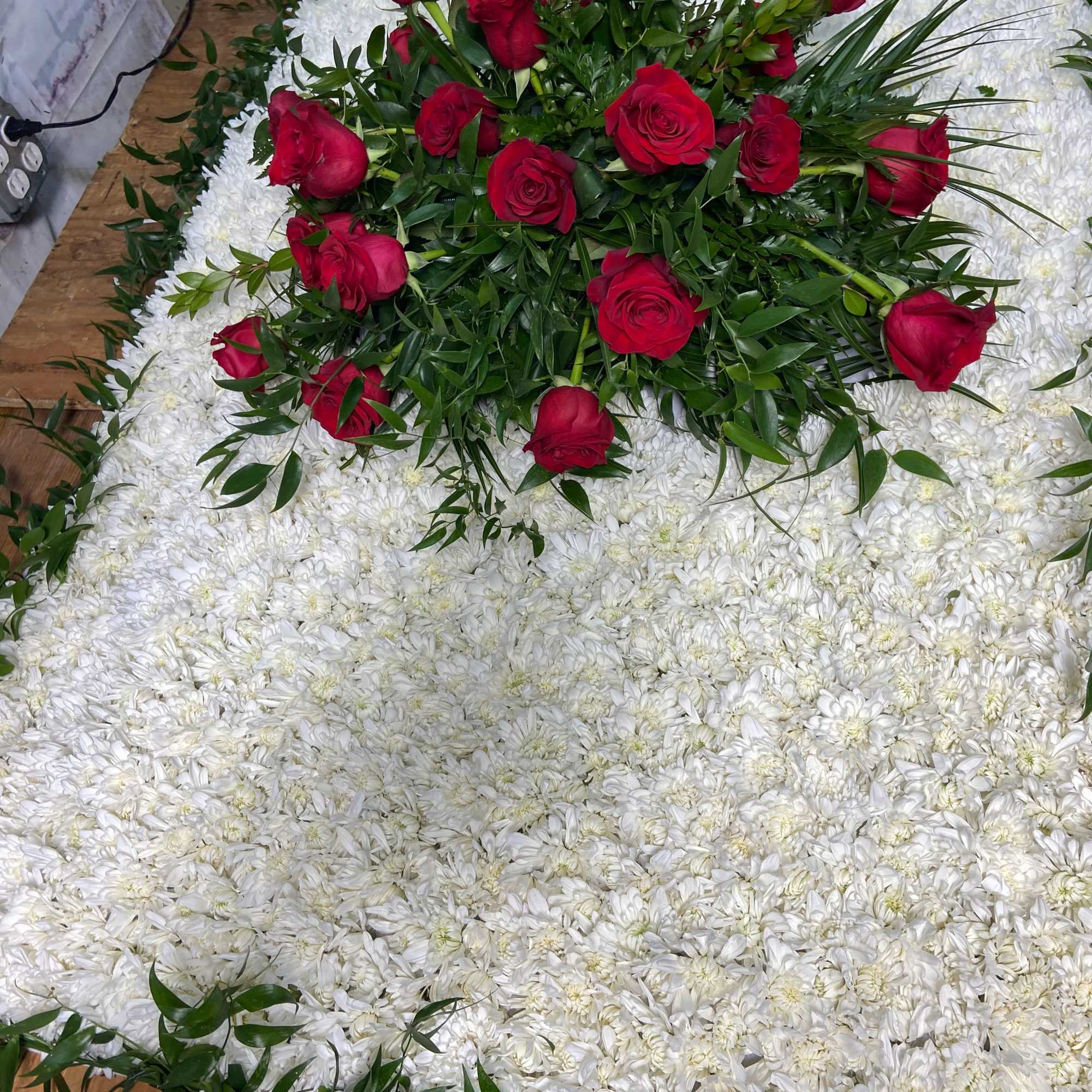 Red roses arranged over a white chrysanthemum floral bed