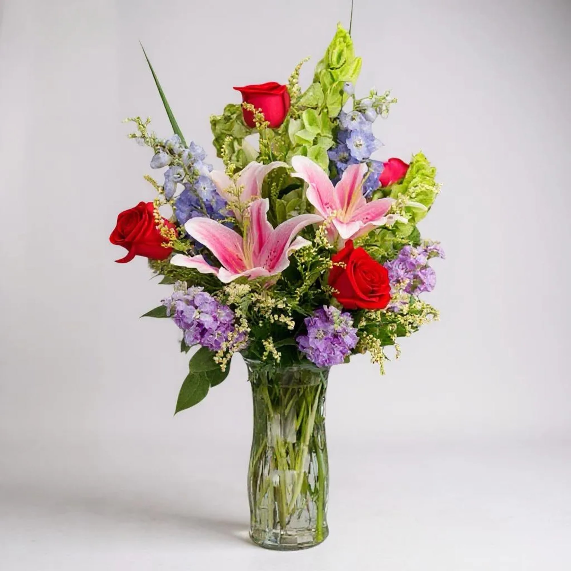 Bouquet of pink lilies and red roses in a clear glass vase
