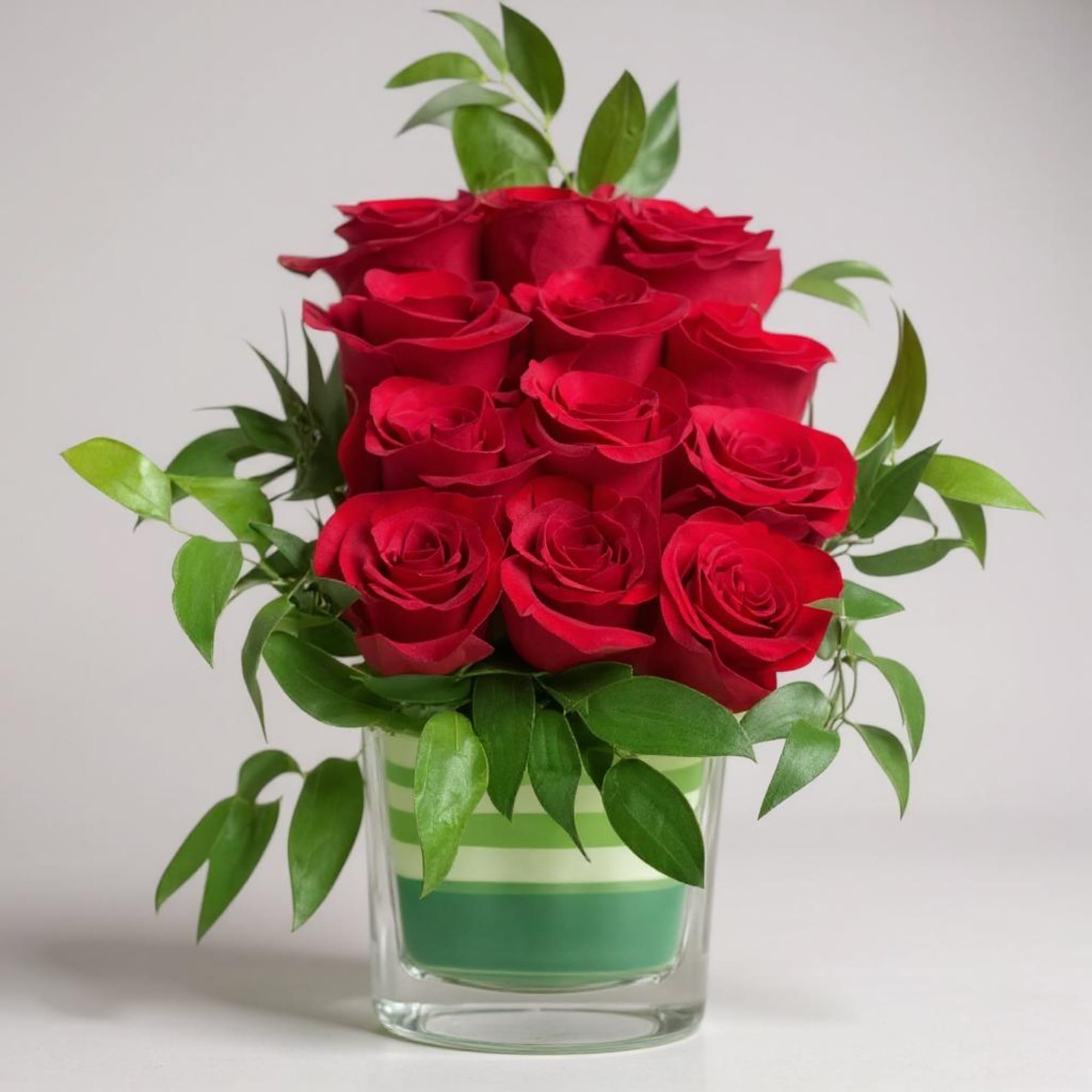 Red roses arranged in a clear glass vase with green foliage