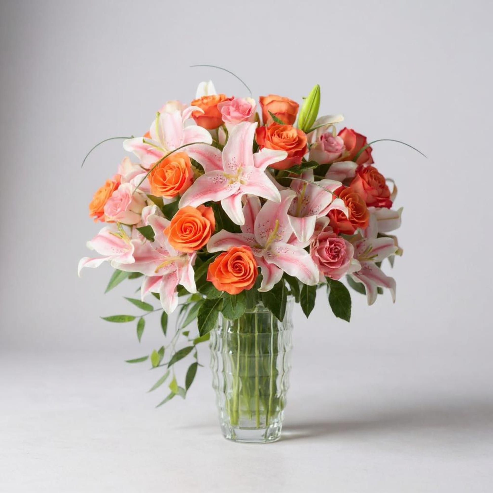 Pink lilies and orange roses arranged in a clear glass vase