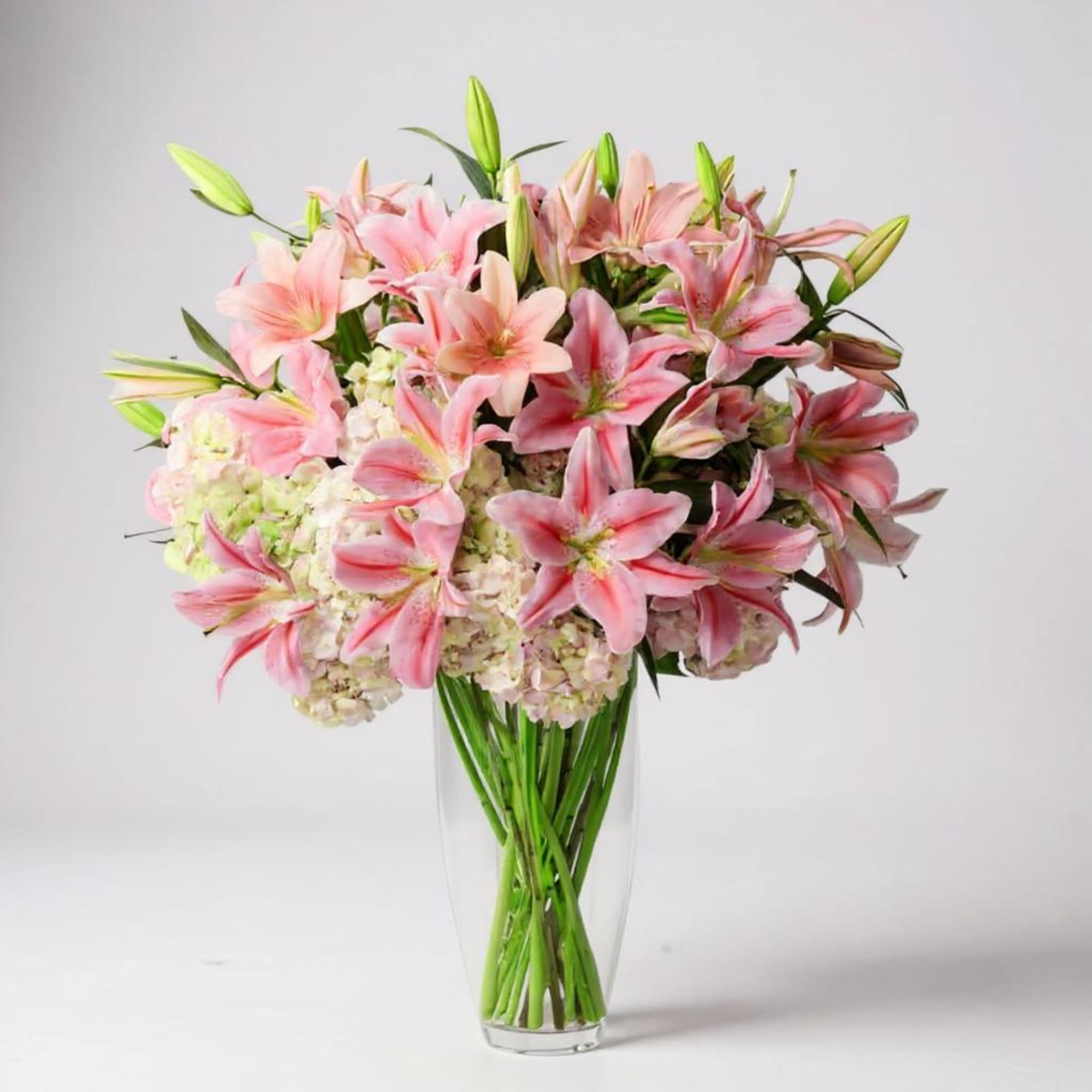 Pink lilies and hydrangeas arranged in a clear glass vase