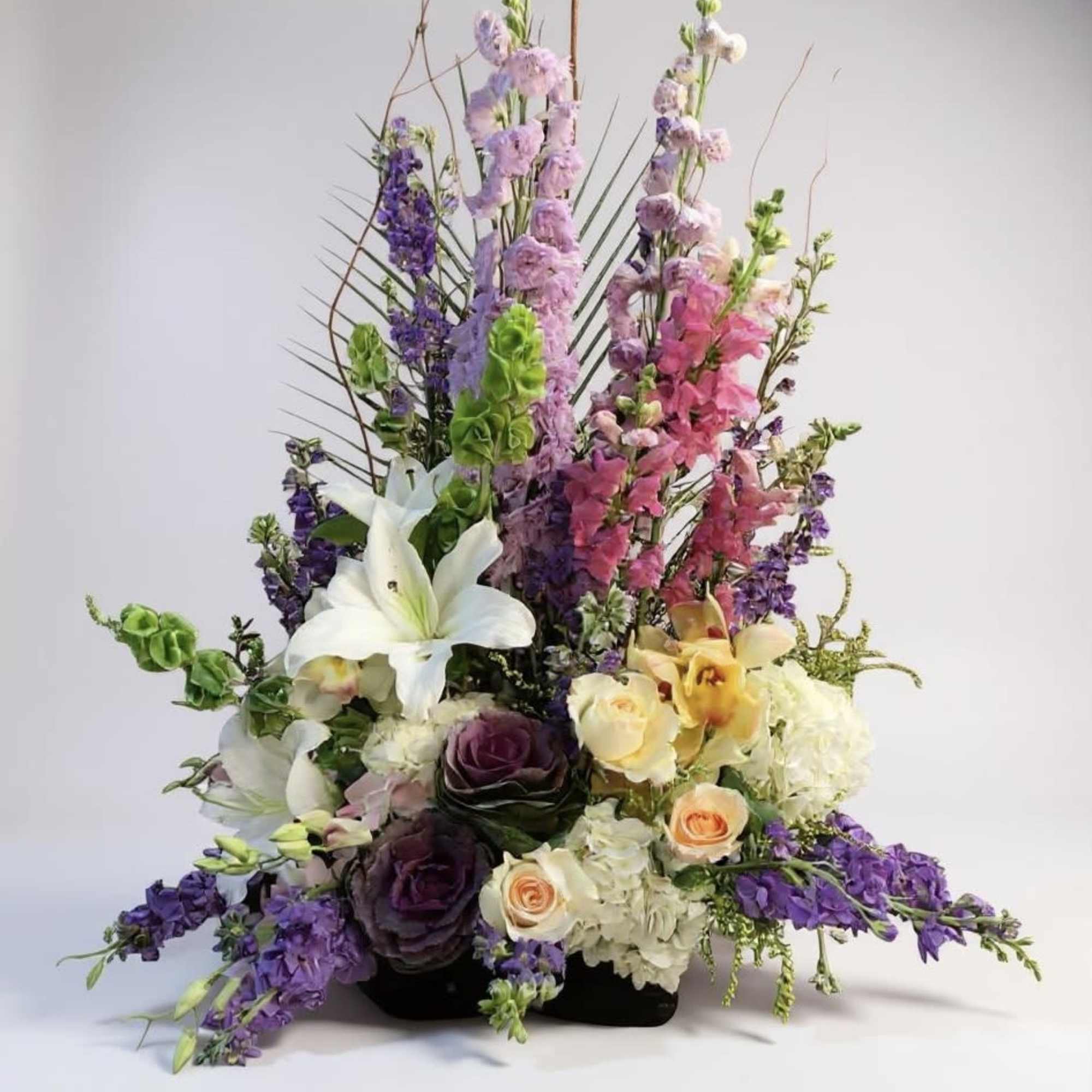 Tall mixed floral arrangement with lilies, roses, and purple blooms