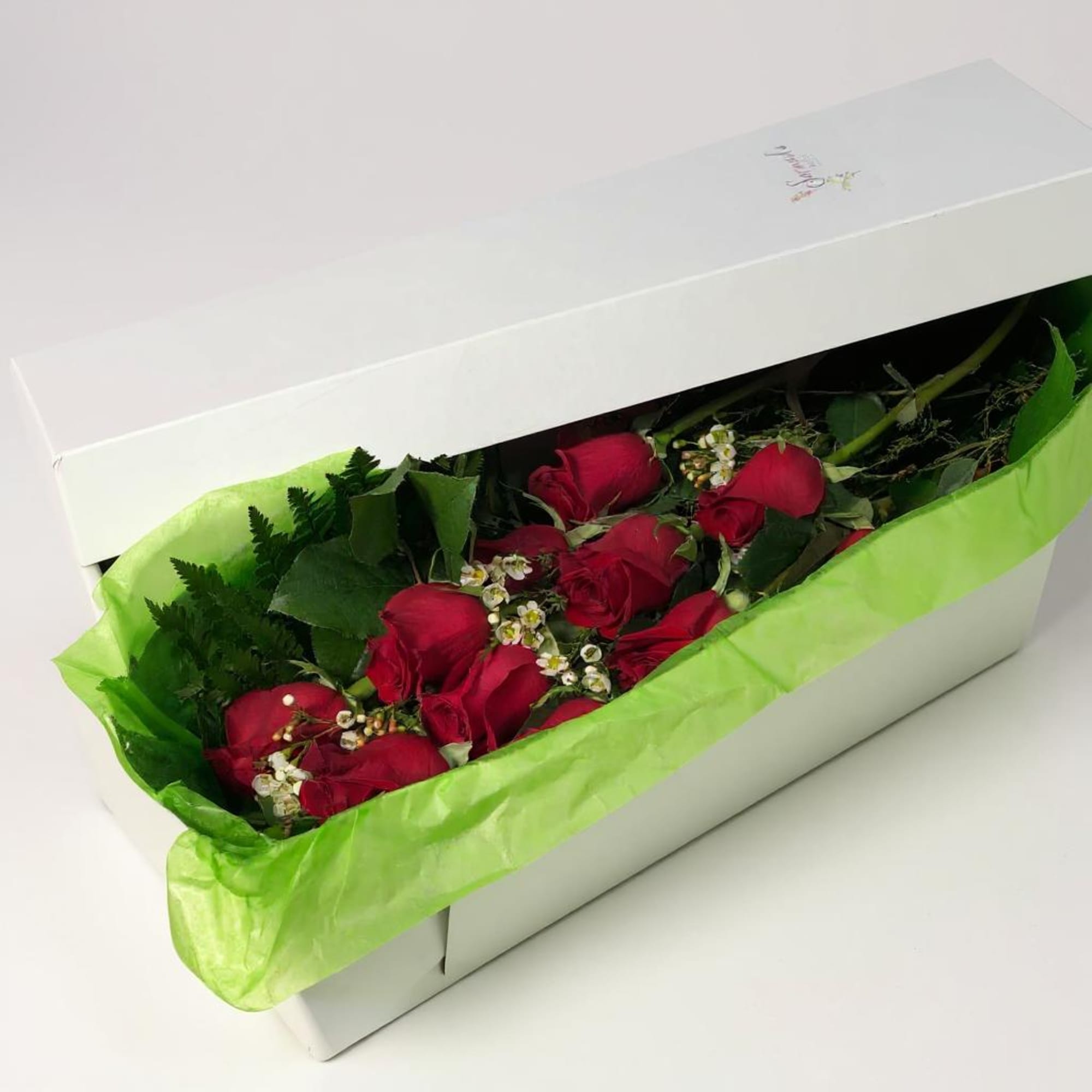 Red roses in a white gift box with green tissue paper