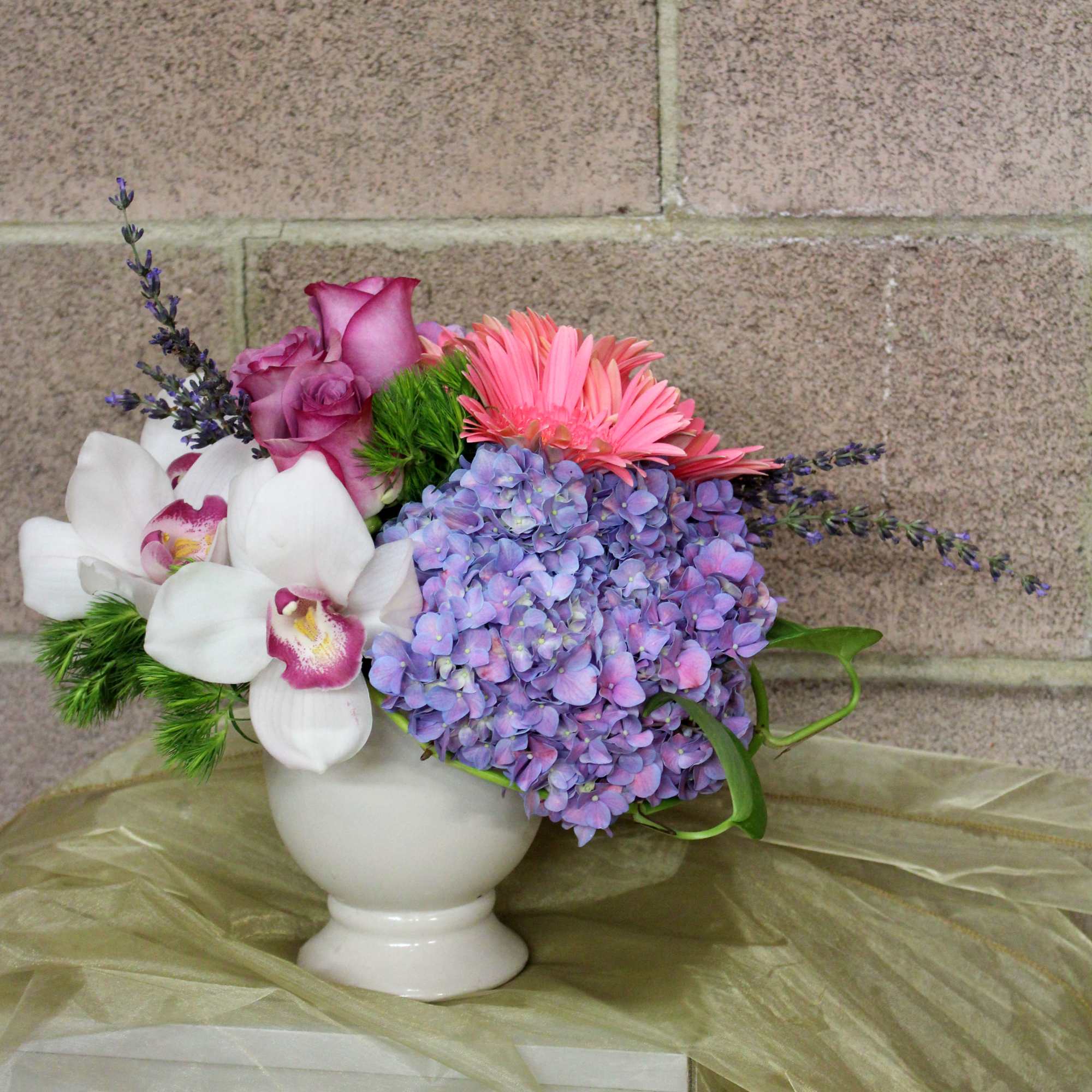 Bouquet of purple roses, pink gerberas, white orchids, and lavender hydrangea in a white vase