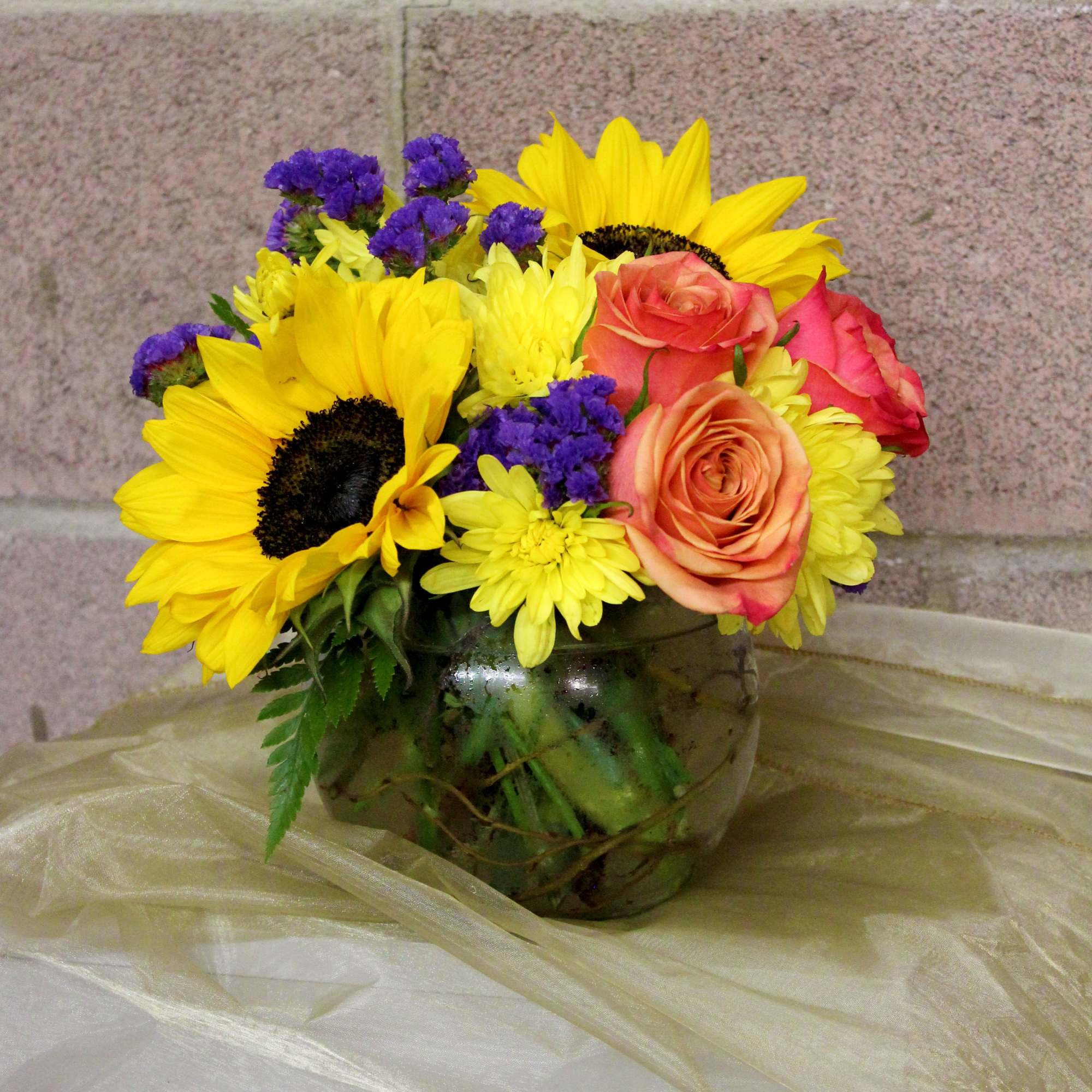 Bouquet of sunflowers, roses, and yellow daisies in a glass vase