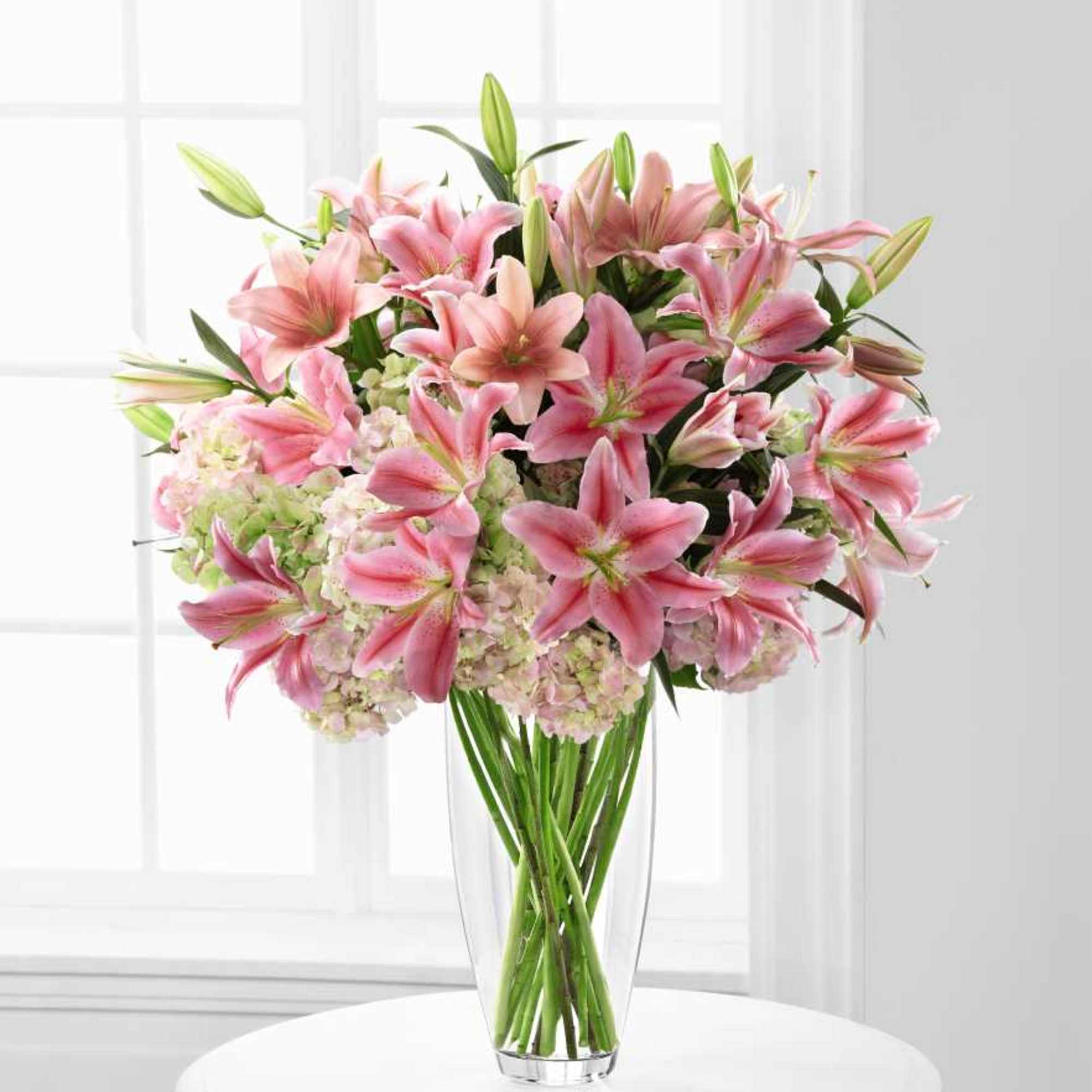 Pink lilies and pale hydrangeas arranged in a clear glass vase