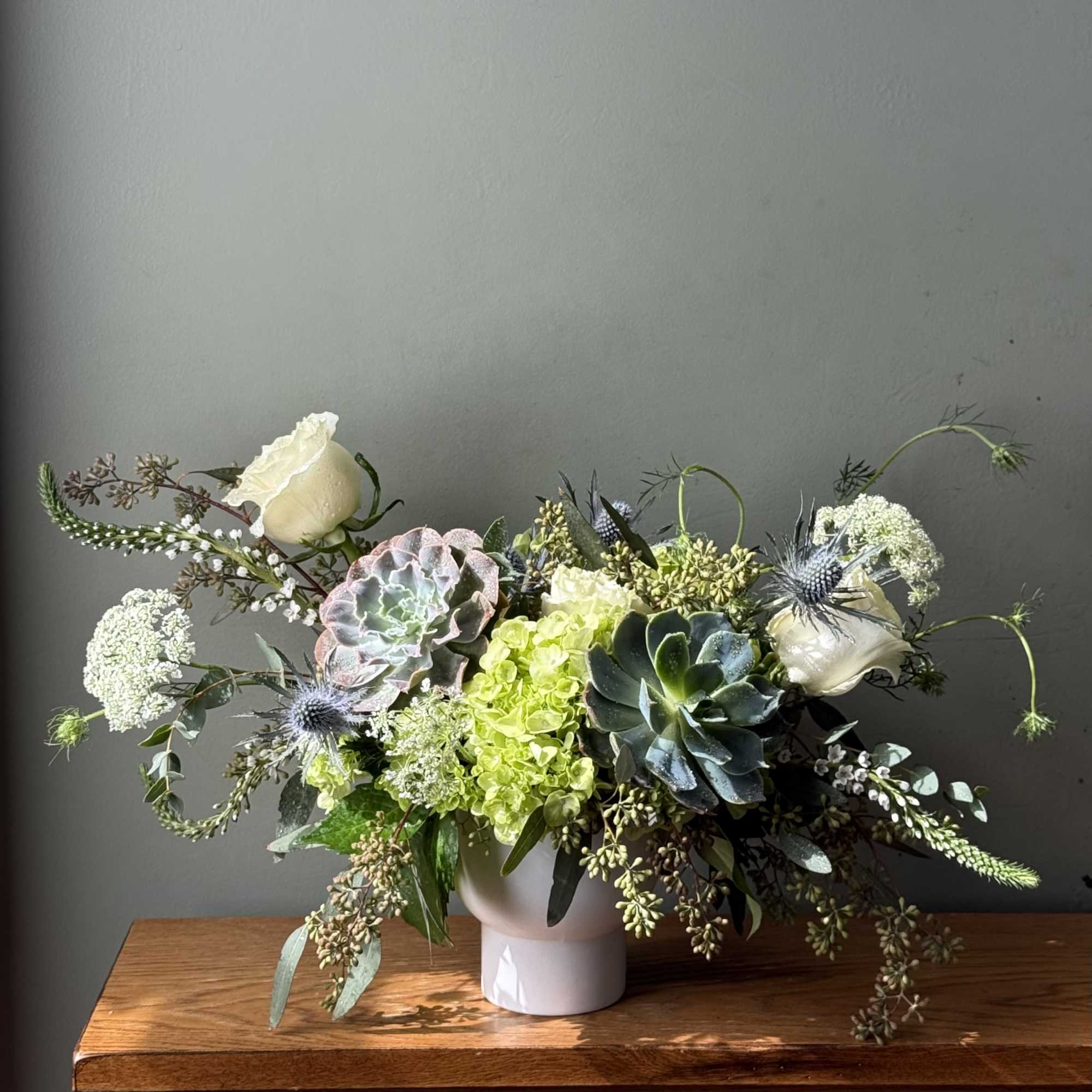 White roses and succulents arranged in a white vase