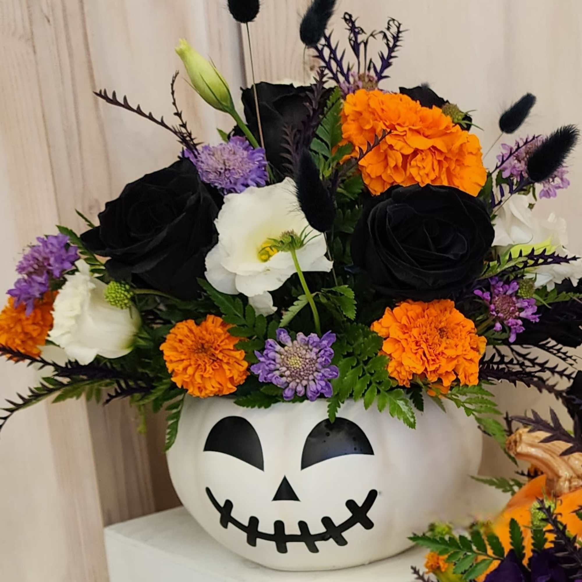 Halloween flower arrangement in a jack-o'-lantern container with black, orange, white, and purple blooms.