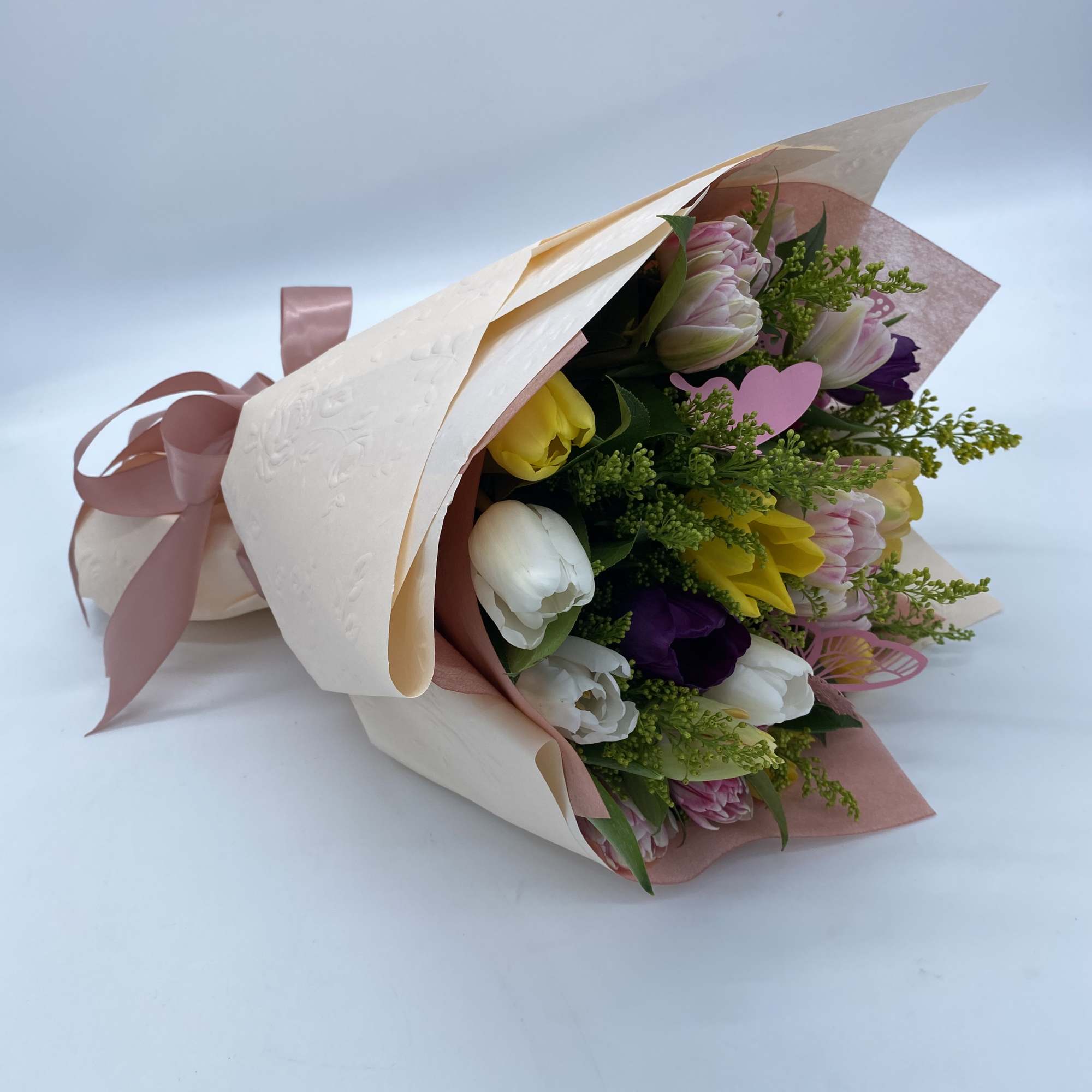 Wrapped bouquet of multicolored tulips with a pink ribbon