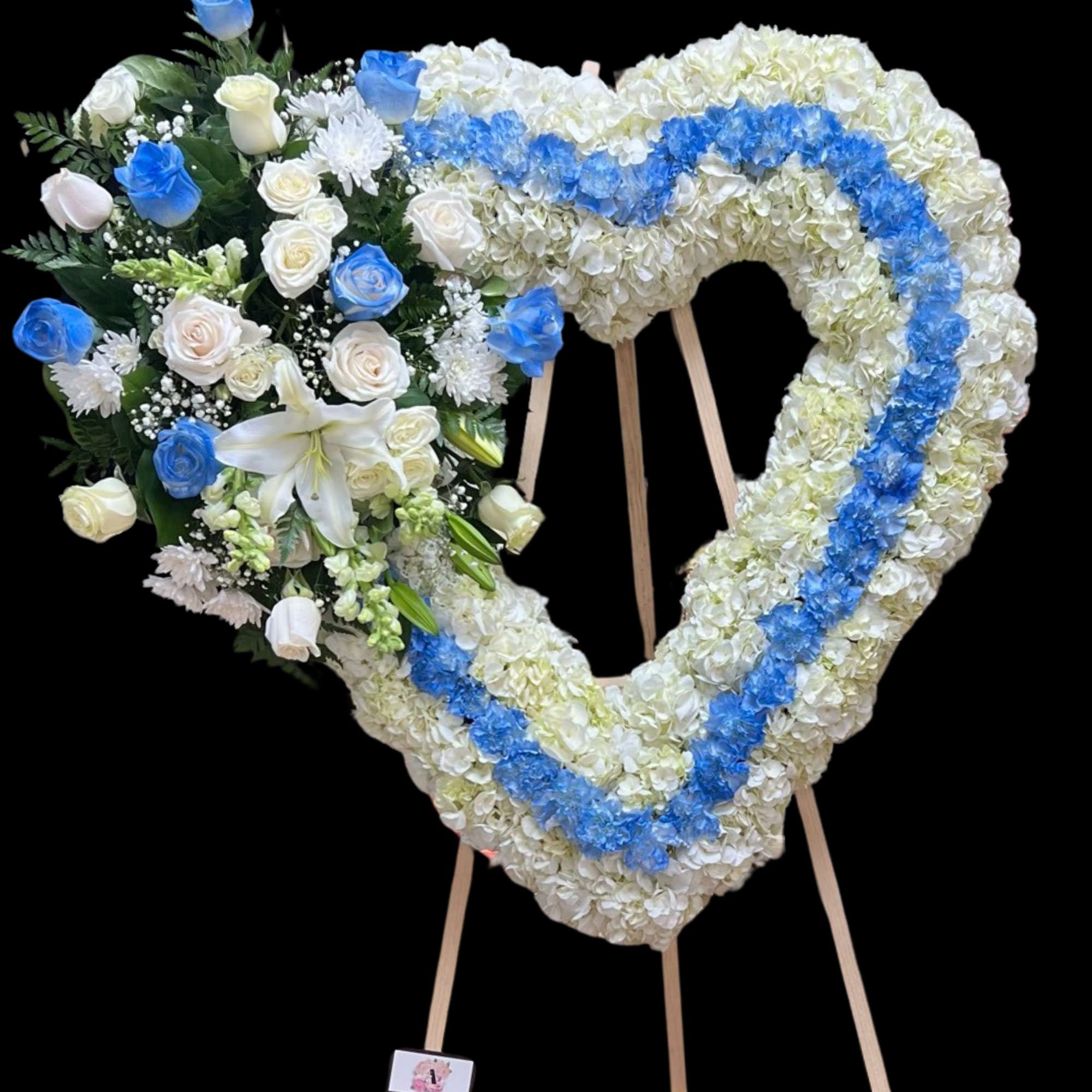 Heart-shaped floral tribute on a stand with white and blue flowers