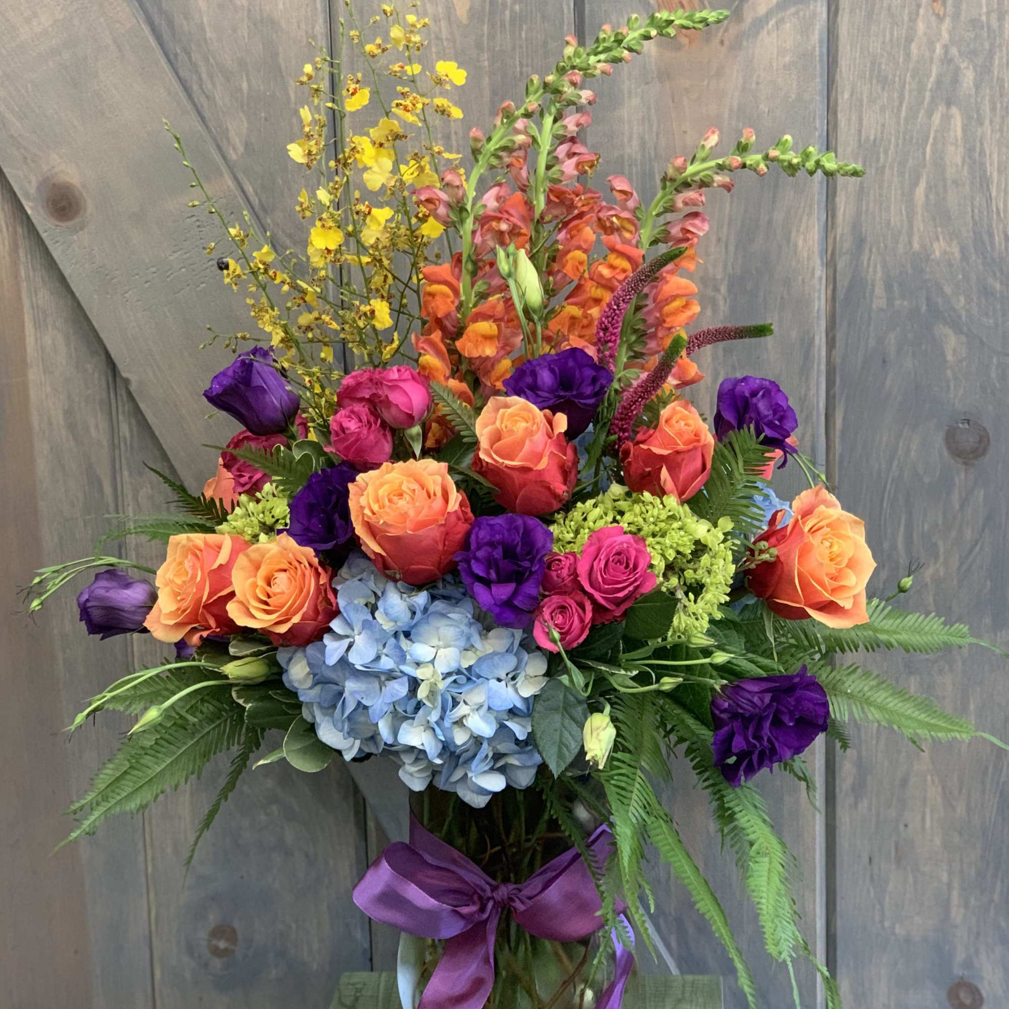 Colorful mixed bouquet in a glass vase with roses, hydrangea, and snapdragons