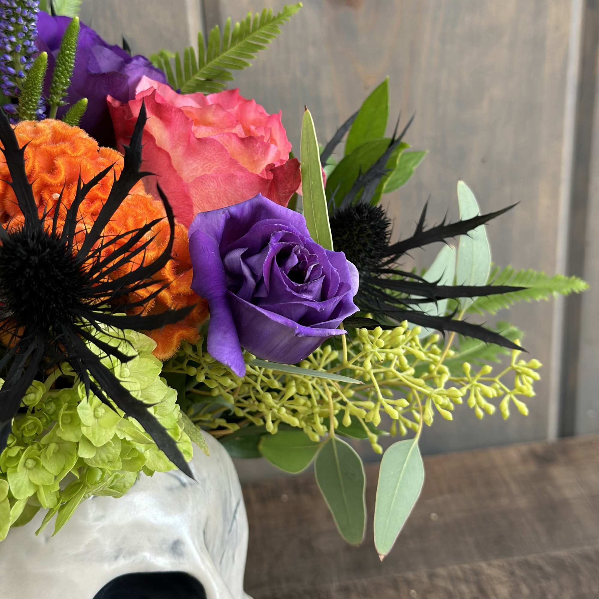Colorful bouquet in a white skull vase with purple and orange roses