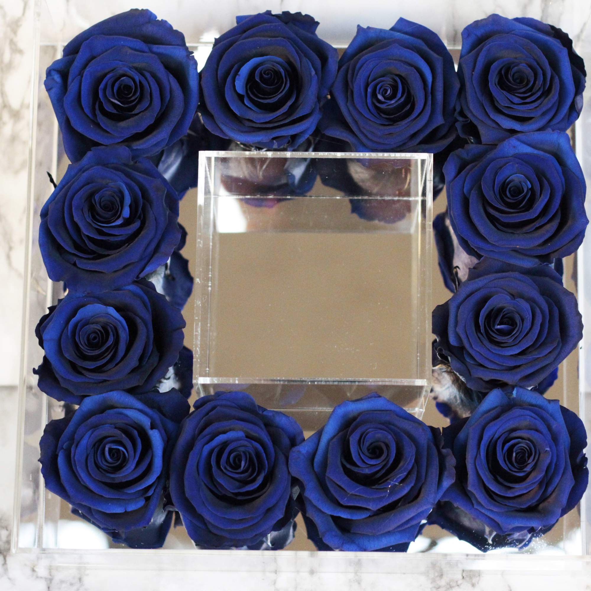 Blue roses arranged in a square clear acrylic box with a mirrored center