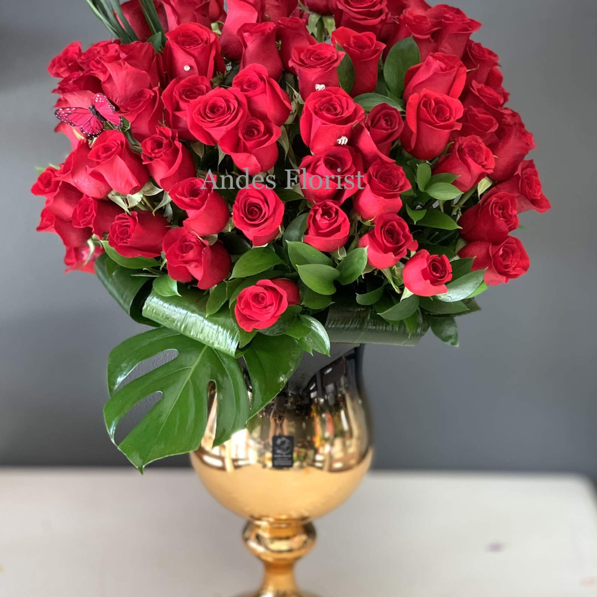 Red rose bouquet in a gold vase with large green leaves