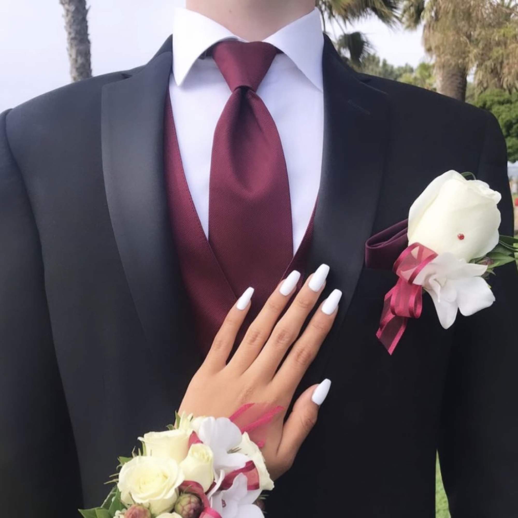 White rose boutonniere and wrist corsage with burgundy ribbon accents