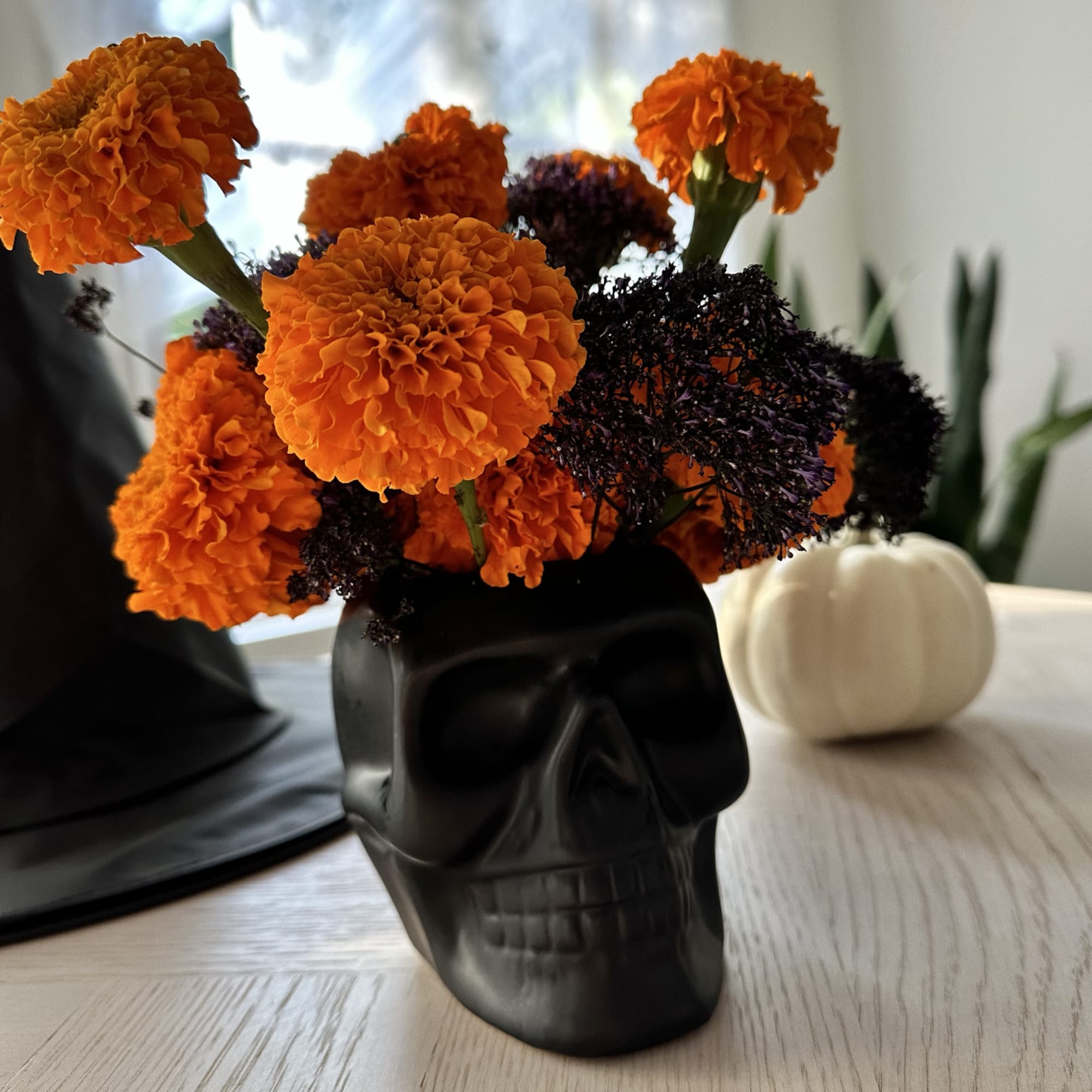 Orange marigolds arranged in a black skull vase with dark filler flowers, photo 5 of 5
