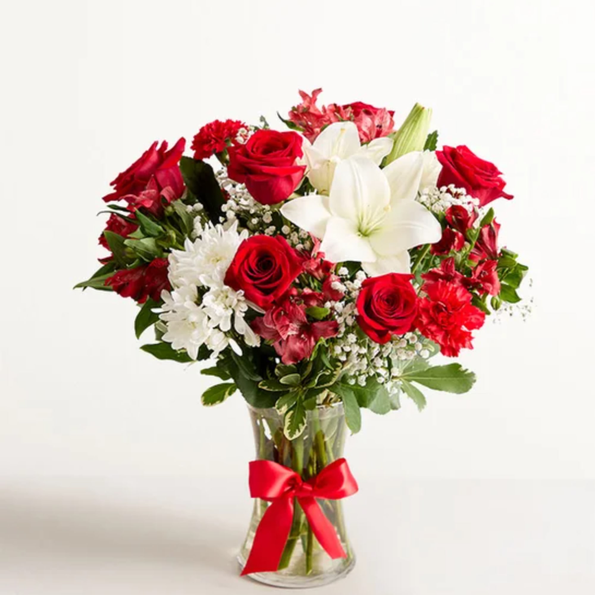 Red roses and white lilies in a clear glass vase with a red ribbon